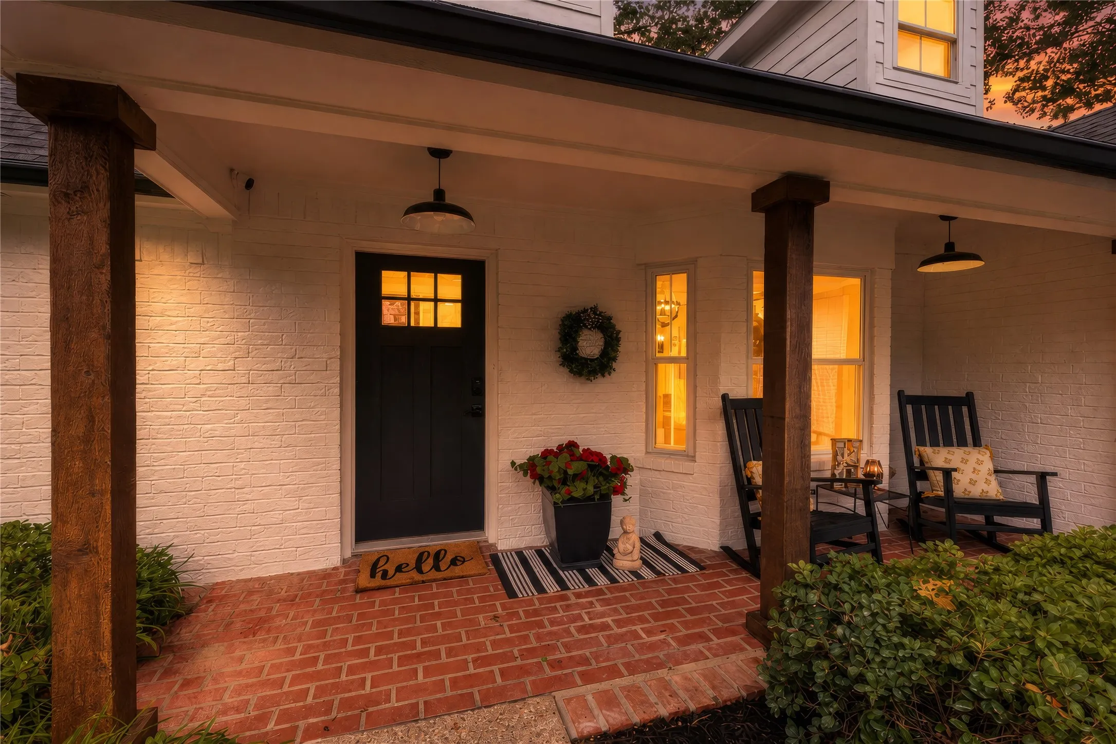 Brick paver porch with dark wood-finish columns, white brick facade, and a dark paneled front door with upper glass lites