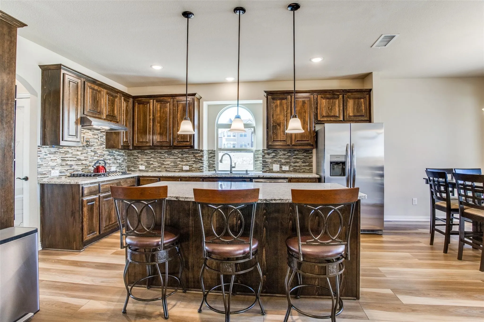 Spacious kitchen featuring an expansive island with pendant lighting, rich wood cabinetry, a mosaic tile backsplash, and stainless steel appliances