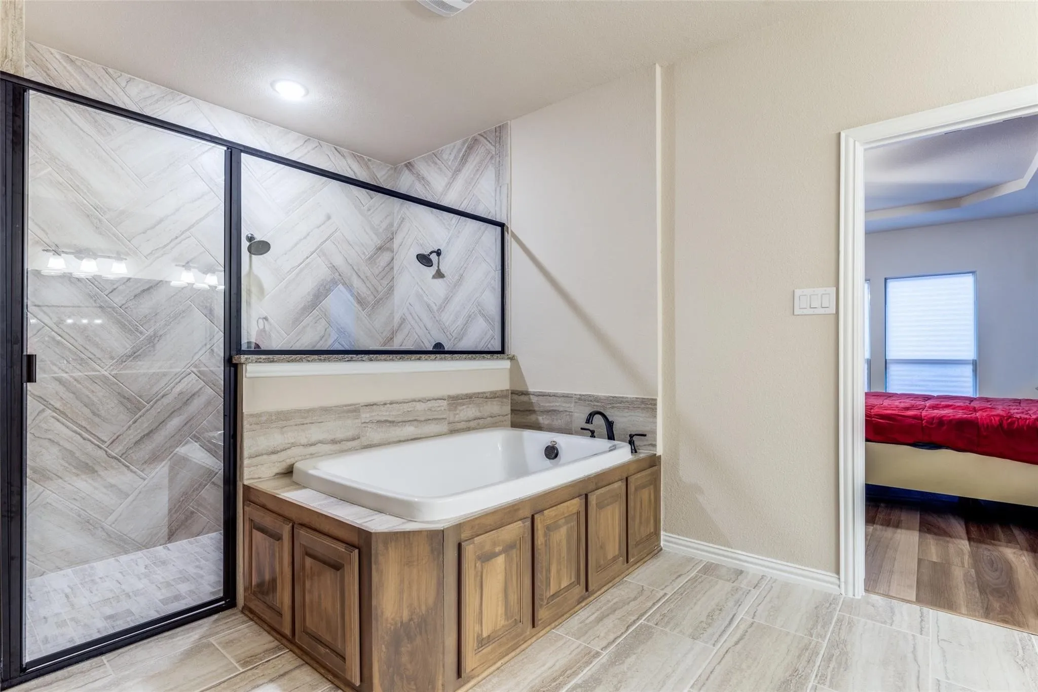 Expansive bathroom featuring a built-in soaking tub with wood-finish paneling, a large shower enclosure with black framing and dual shower heads, and an integrated shower bench