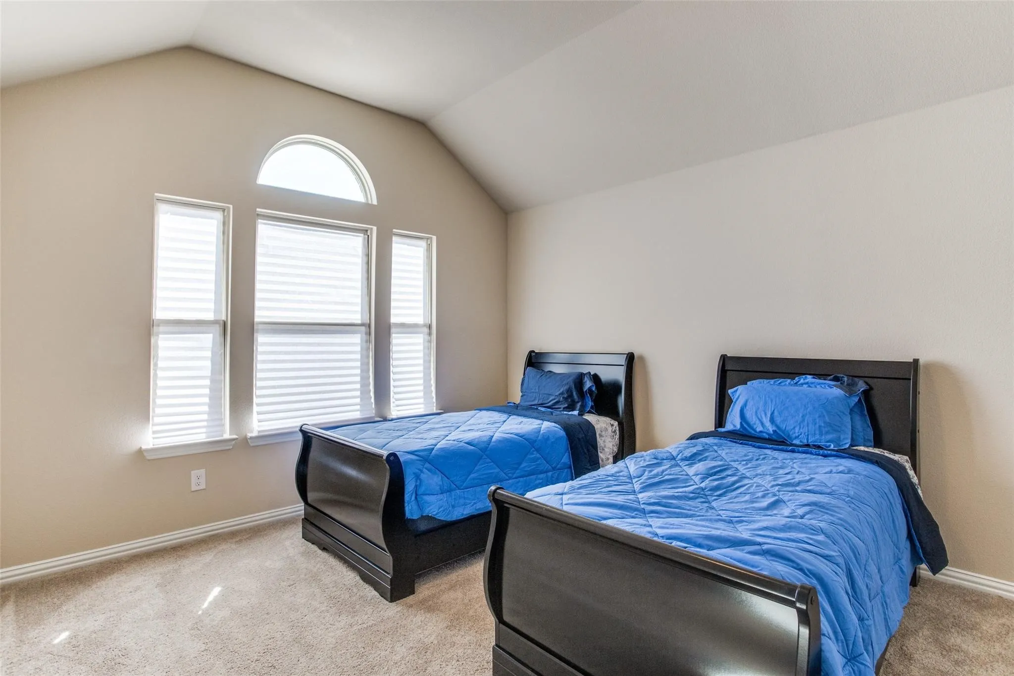 Vaulted ceiling room featuring multiple windows including an arched transom, neutral wall tones, and carpeted flooring