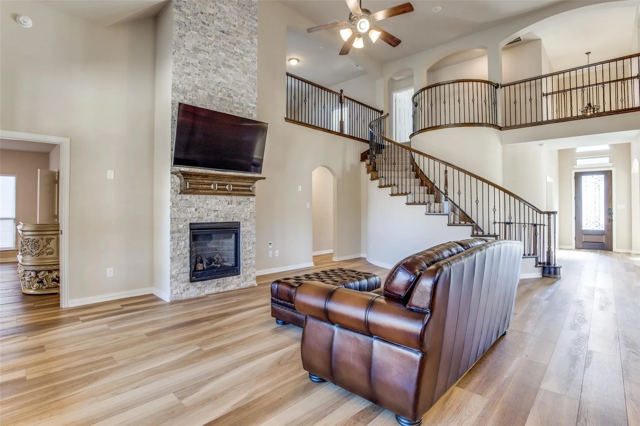 Two-story living area featuring a stone-clad fireplace with a wood mantel, a gas log insert, and wood-finish flooring