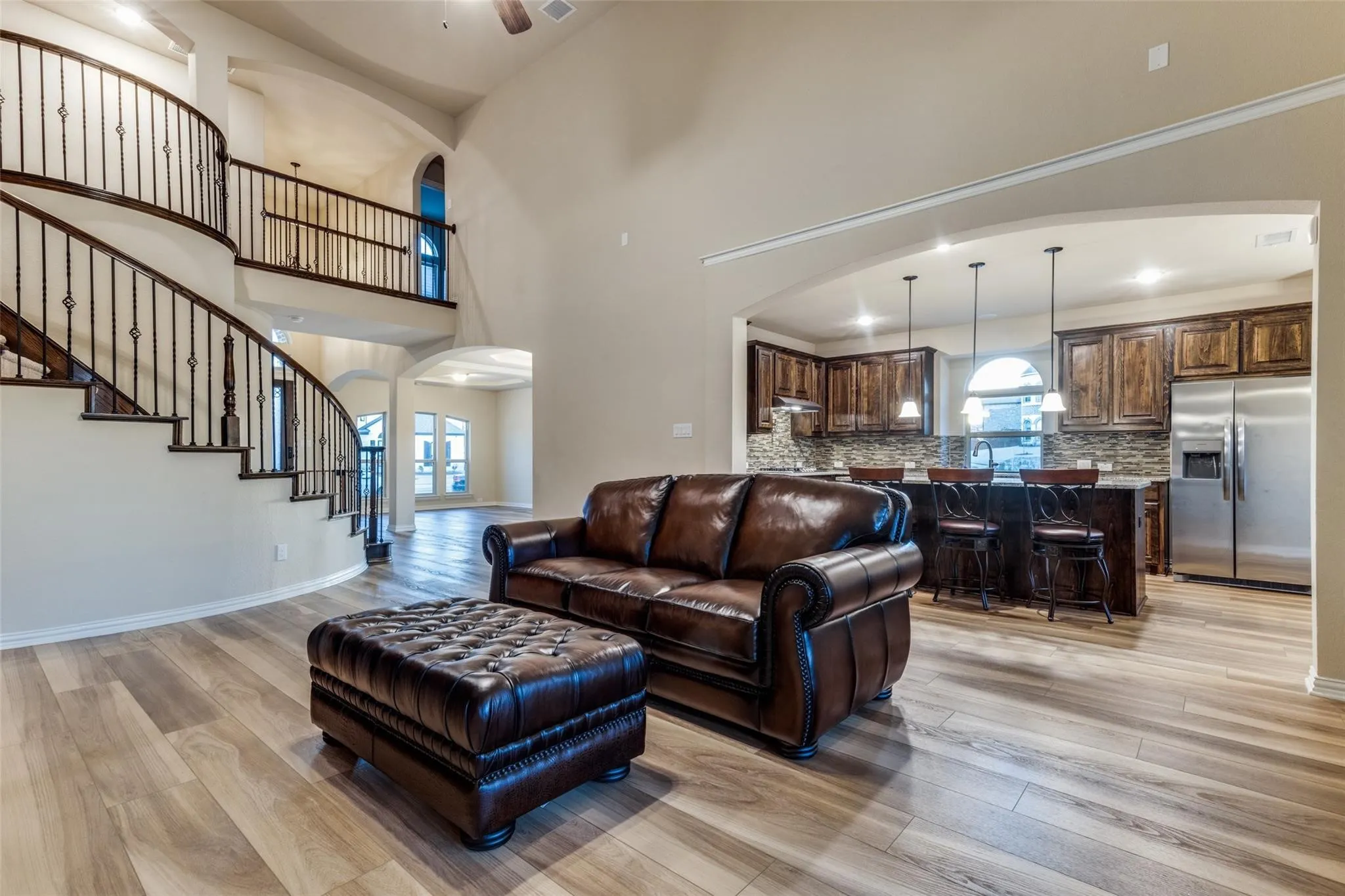 Two-story living area featuring a grand staircase with wrought iron balusters, high ceilings, wood-finish flooring, and an open concept kitchen with dark wood cabinetry and stainless steel appliances