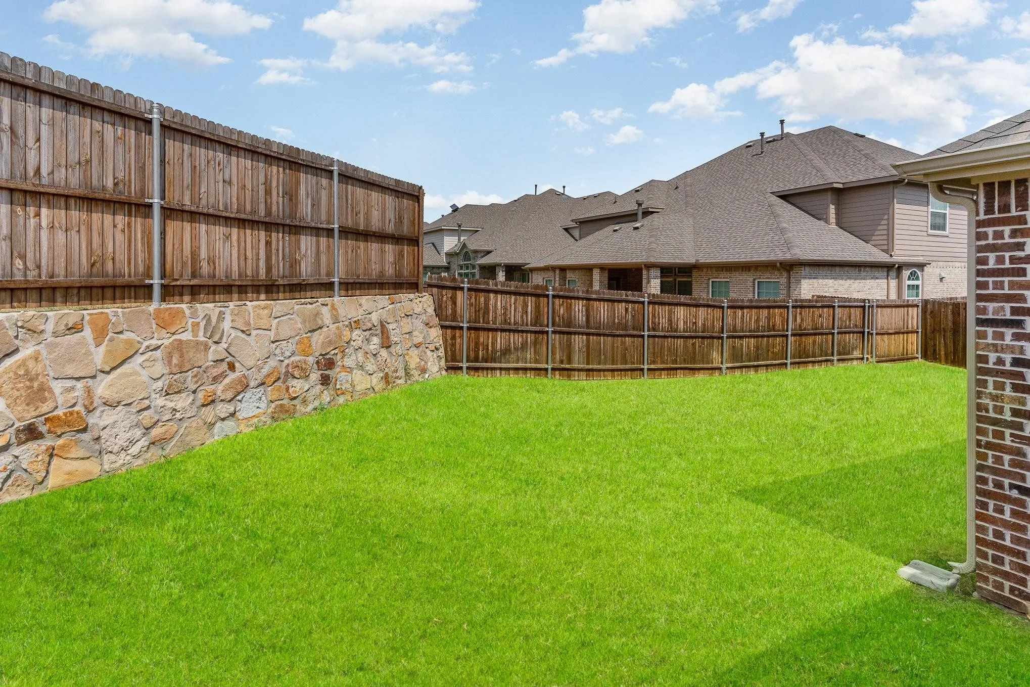 Expansive backyard featuring a lush lawn, a natural stone retaining wall, and a wooden privacy fence