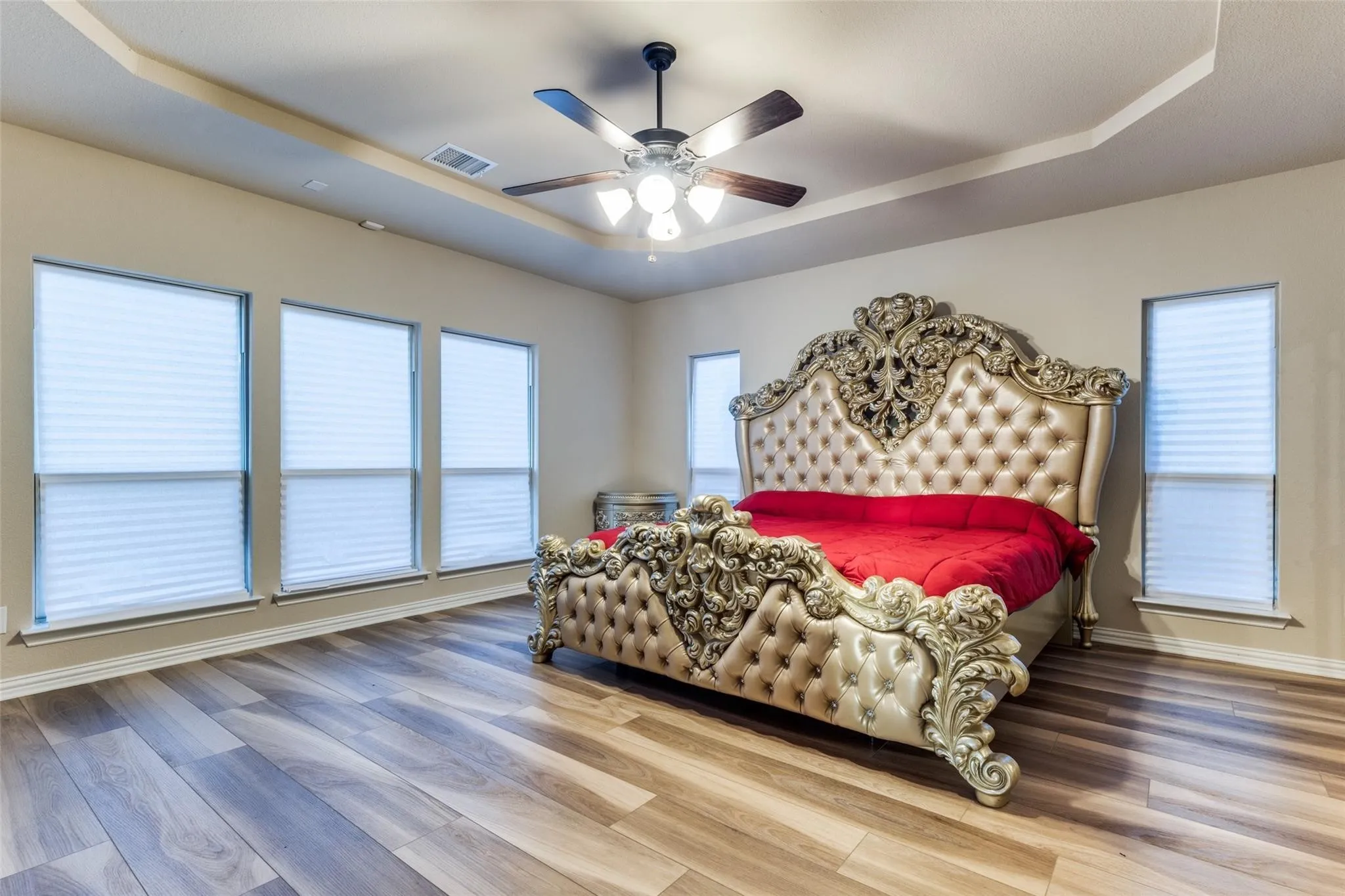 Spacious room featuring wood-finish flooring, a tray ceiling, and a ceiling fan with integrated lighting