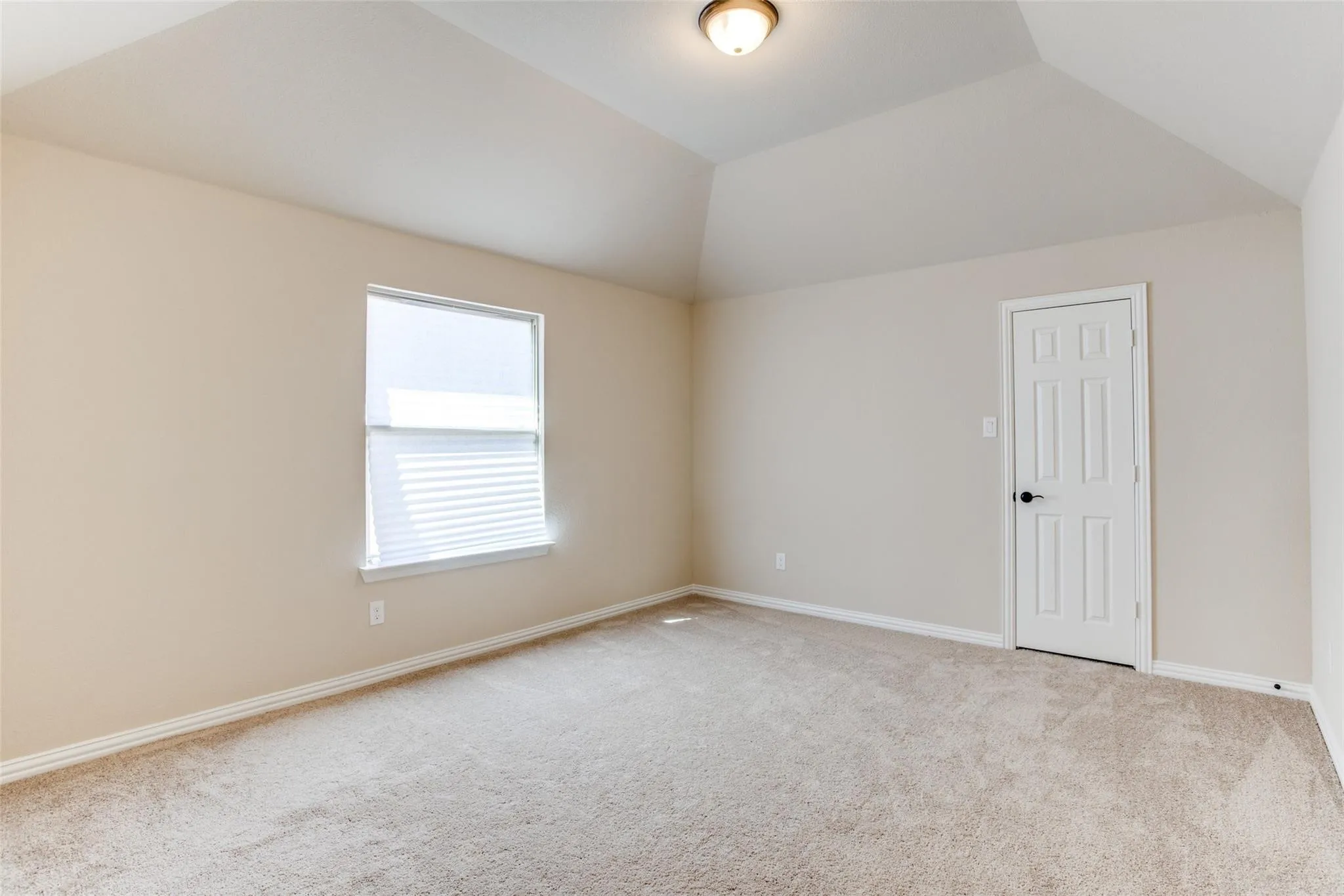 Carpeted interior space featuring a vaulted ceiling and neutral wall tones