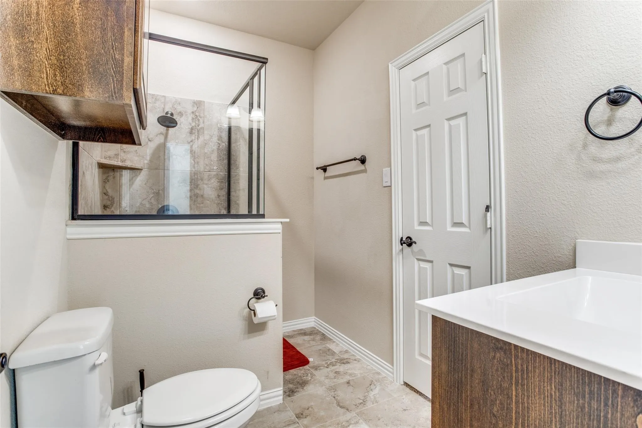 Bathroom featuring a tiled shower with a glass enclosure, wood-finish vanity with a white countertop, and neutral wall paint