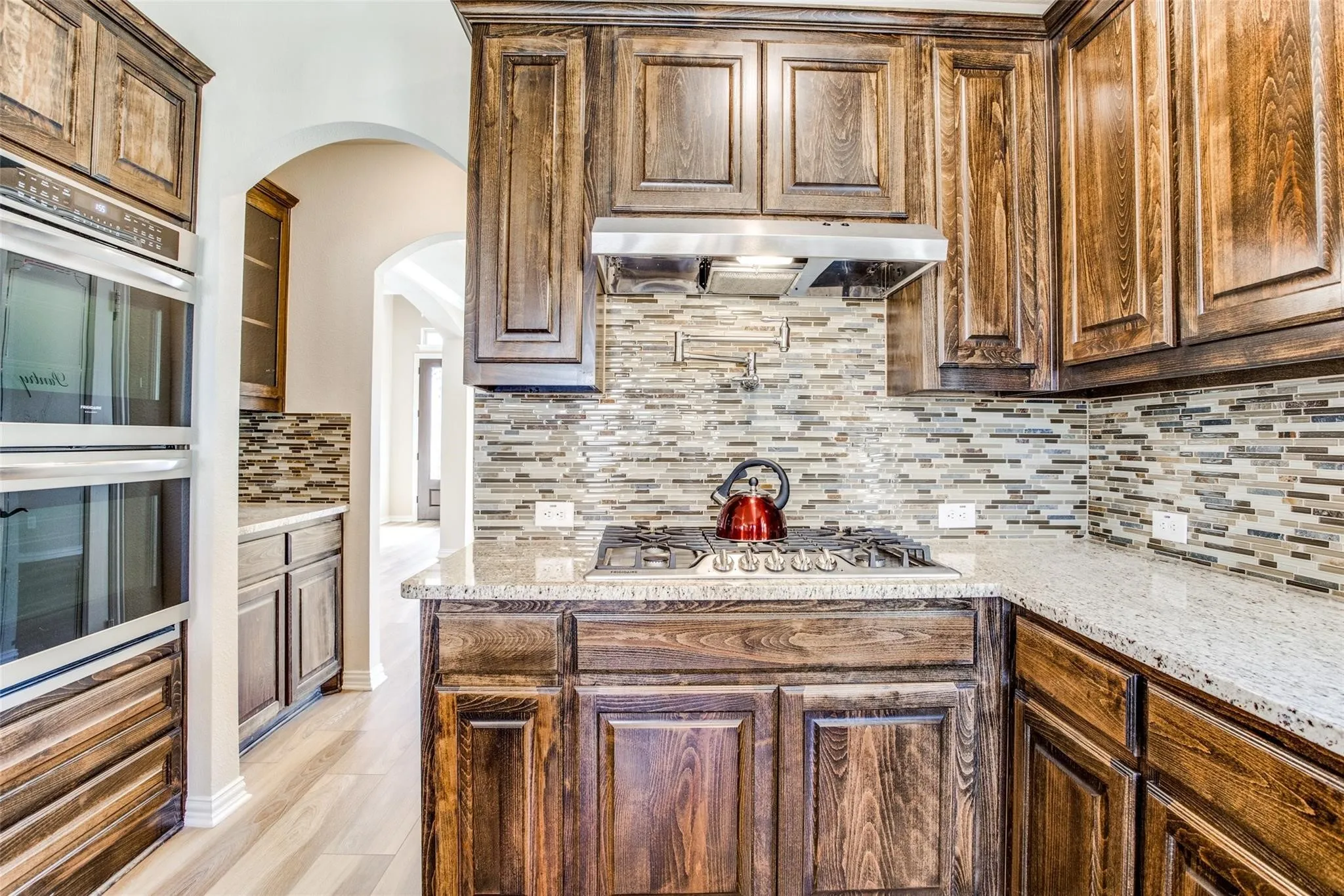 Kitchen featuring rich wood cabinetry, stainless steel appliances, a mosaic tile backsplash, a gas cooktop, and light-toned countertops
