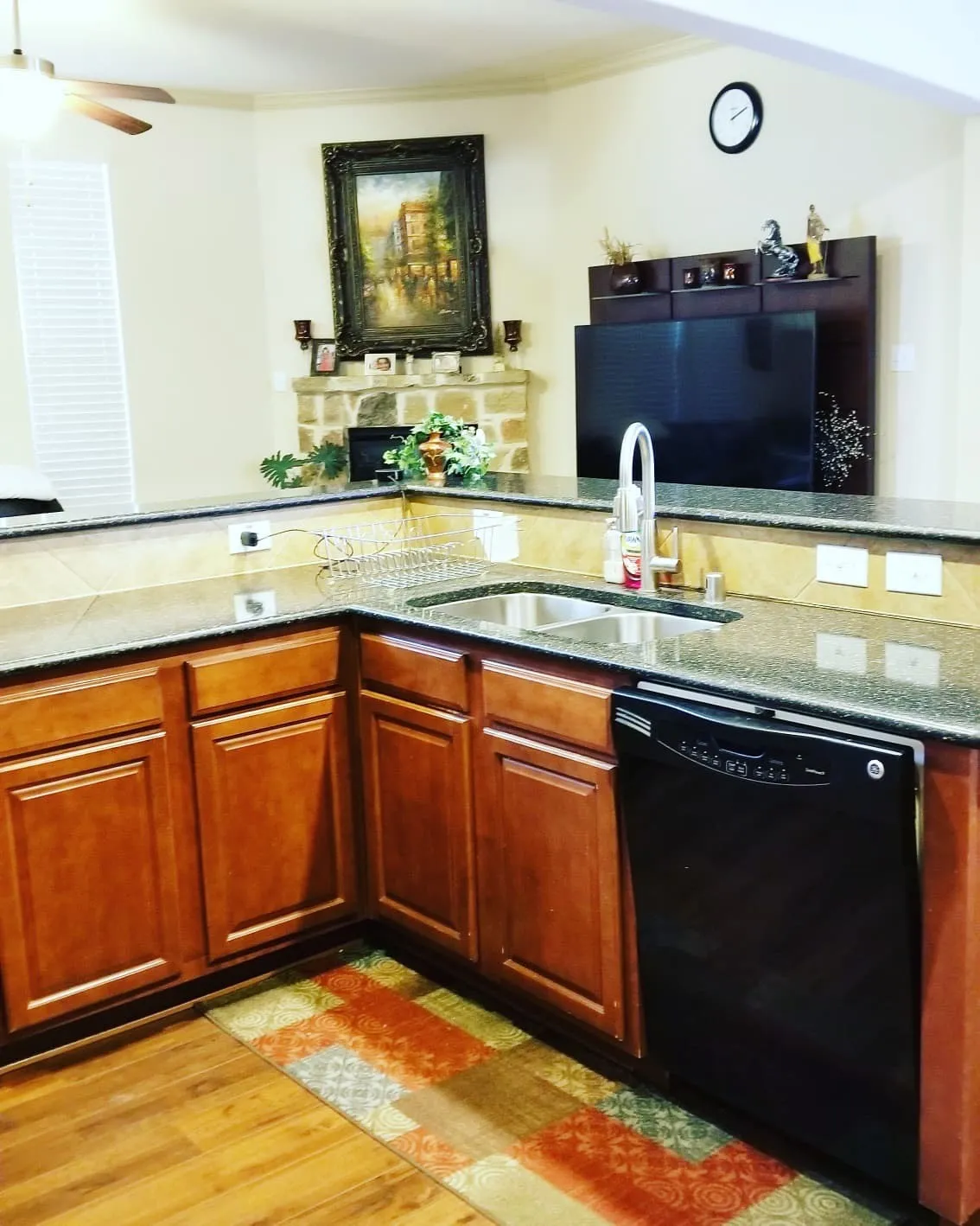 Kitchen featuring granite-style countertops, wood-finish cabinetry, stainless steel sink with a high-arc faucet, and black dishwasher