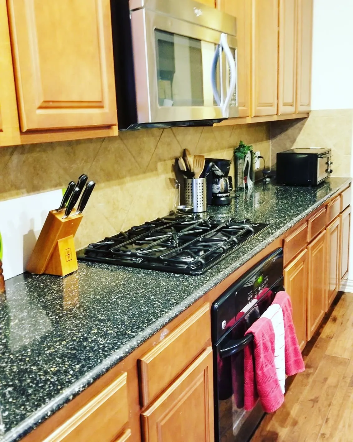Kitchen featuring a gas range, built-in oven, stainless steel microwave, stone-finish countertops, and light wood cabinetry