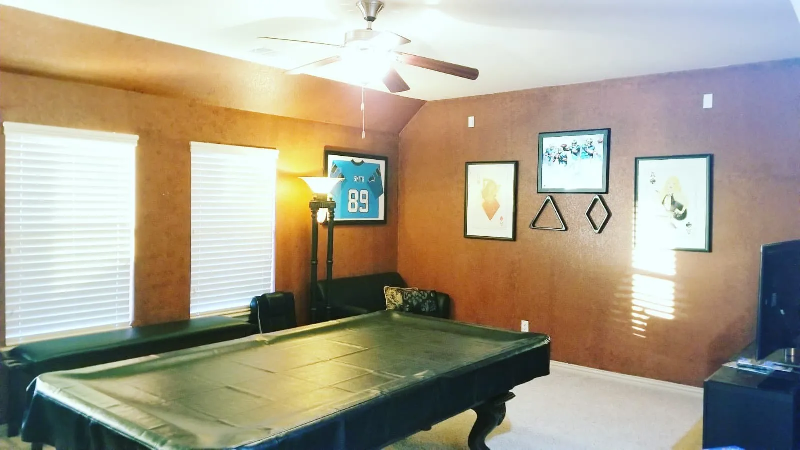 Spacious room featuring textured walls, two windows with horizontal blinds, and a ceiling fan with integrated lighting