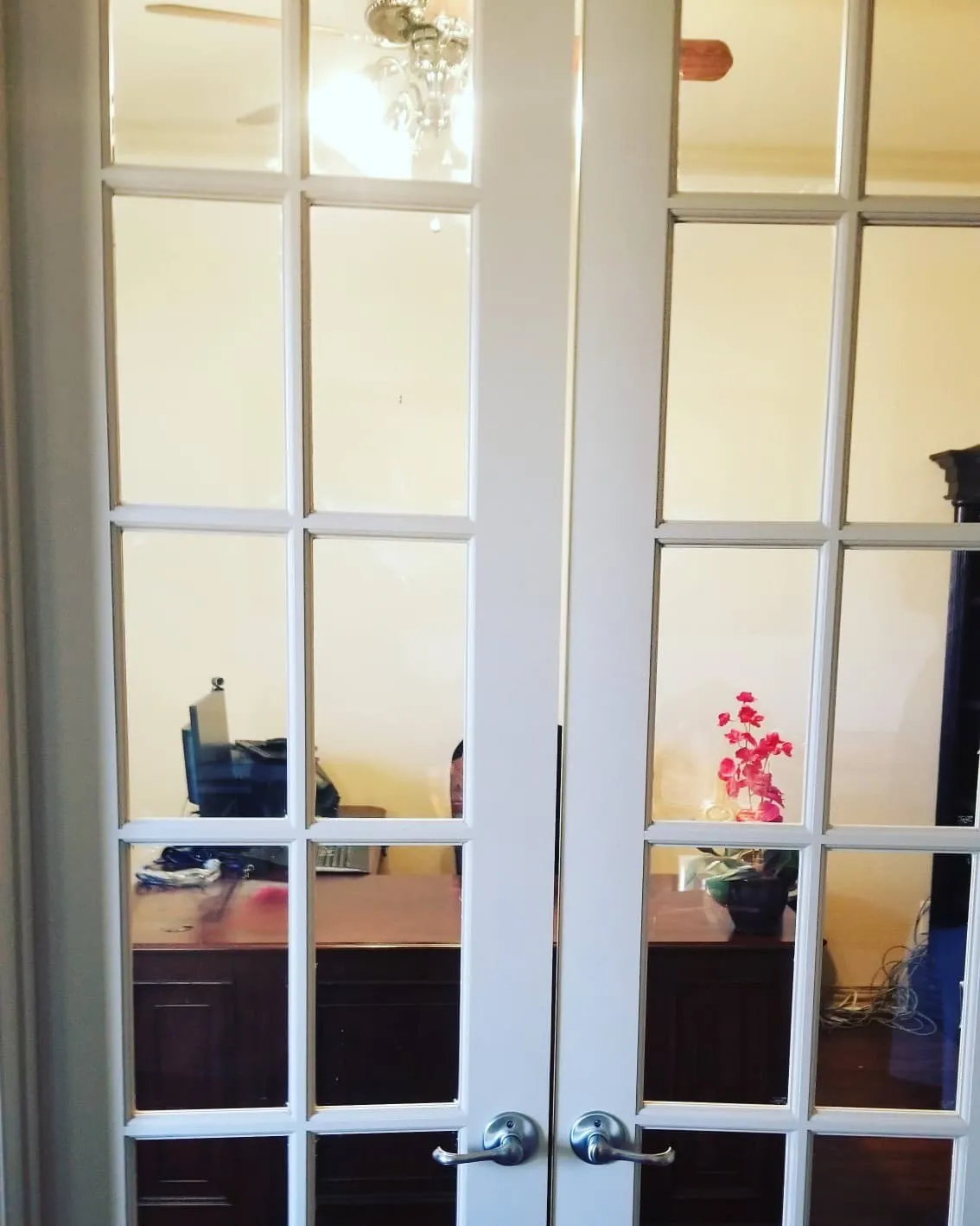 White French doors with clear glass panels open to a room featuring a dark wood-finish desk and a ceiling fan with a chandelier light fixture