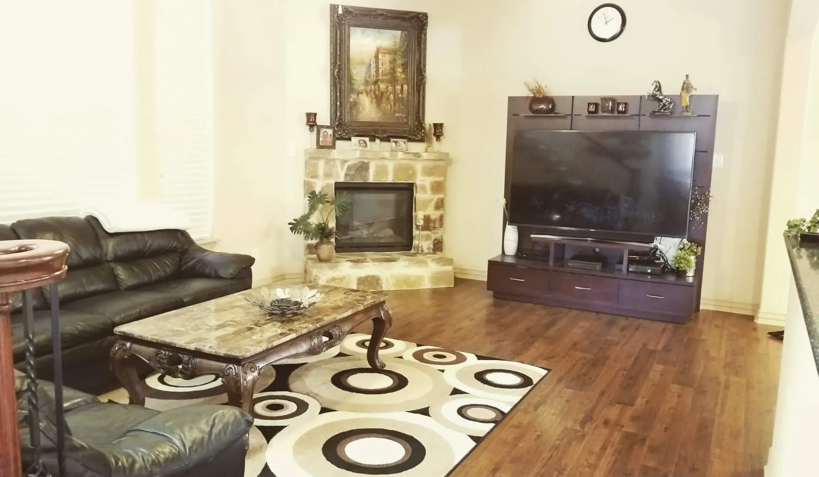 Living area featuring a stone-clad fireplace with a hearth, wood-finish flooring, and white walls