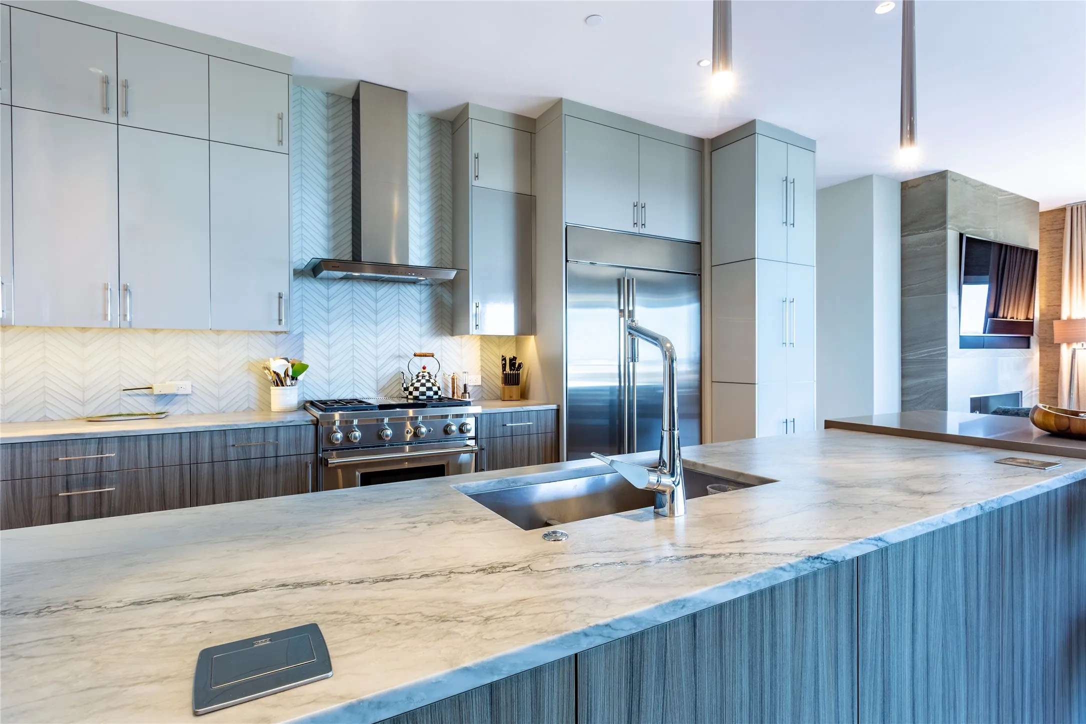White Pearl Aria leathered stone counters with concealed electrical pop-ups. Palms pattern backsplash.