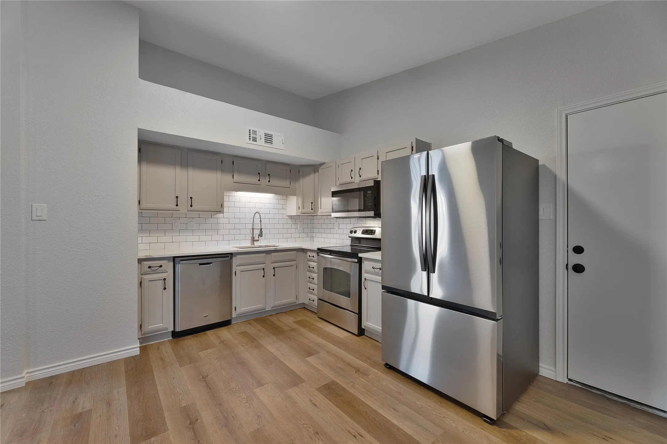 Kitchen featuring wood-finish flooring, white subway tile backsplash, stainless steel appliances, and light-toned cabinetry with dark hardware