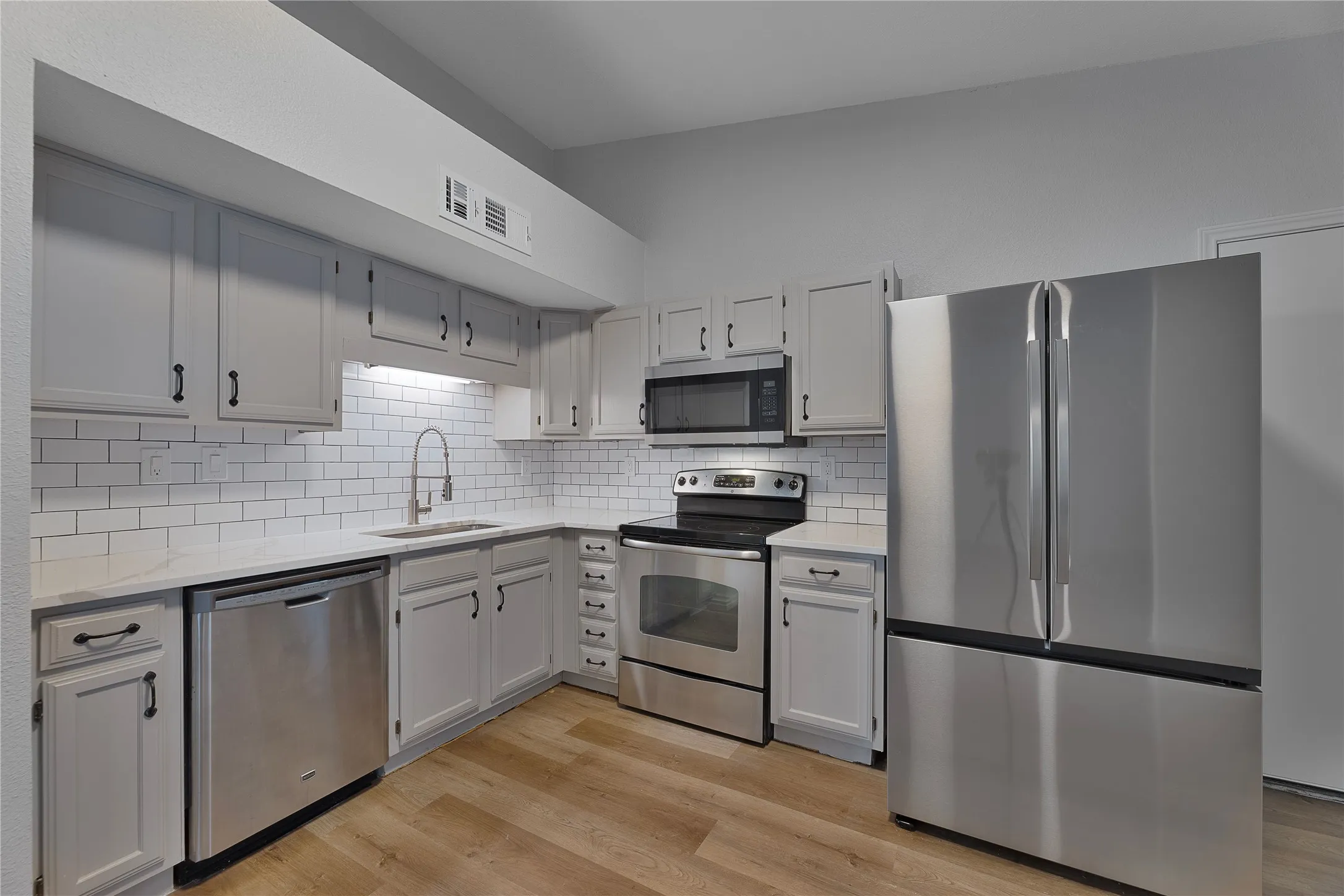 Kitchen featuring light-toned cabinetry, stainless steel appliances, a white subway tile backsplash, light countertops, and wood-finish flooring