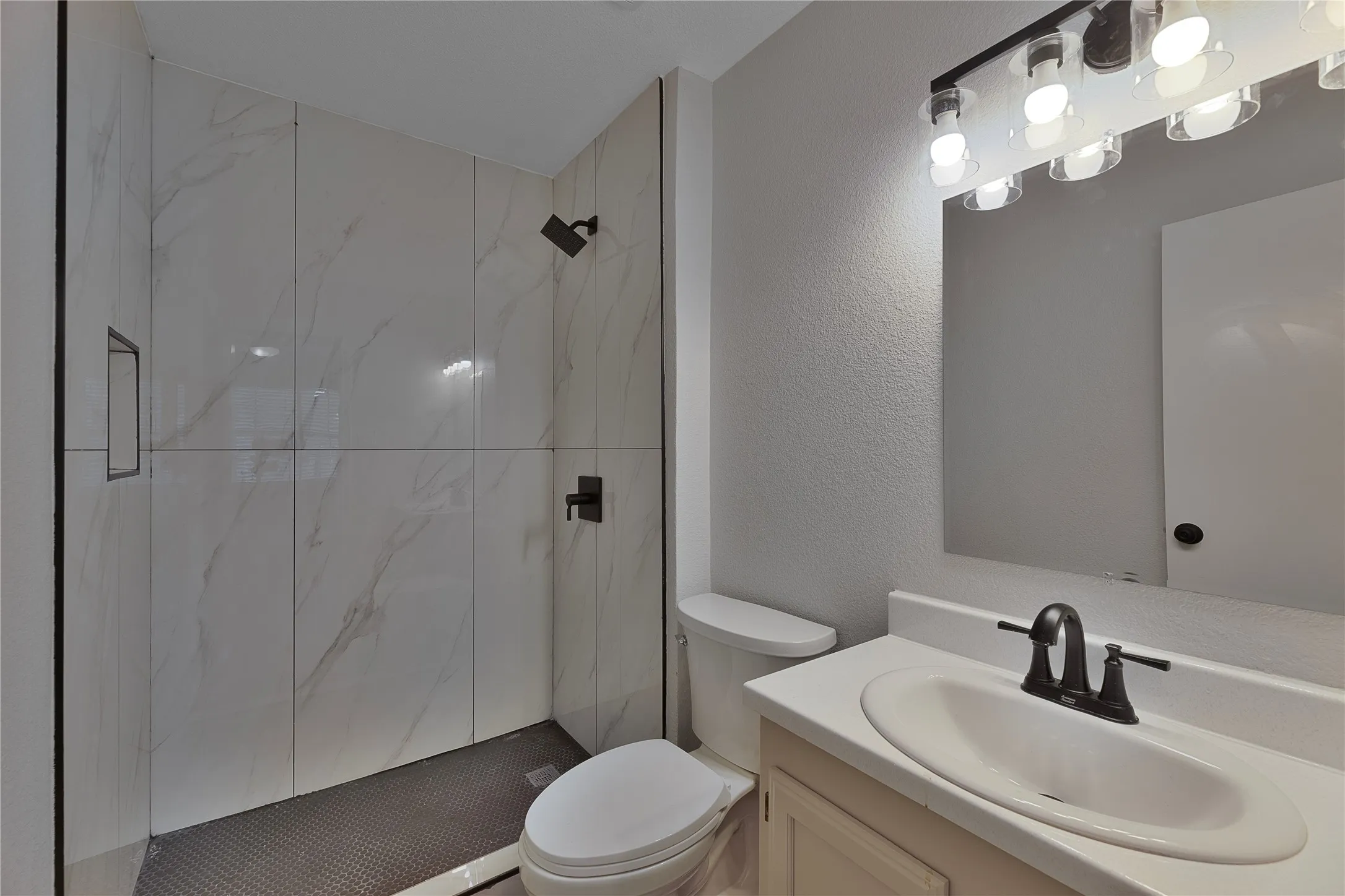Shower stall with white marble-style wall tiles, dark floor tiles, and matte black fixtures