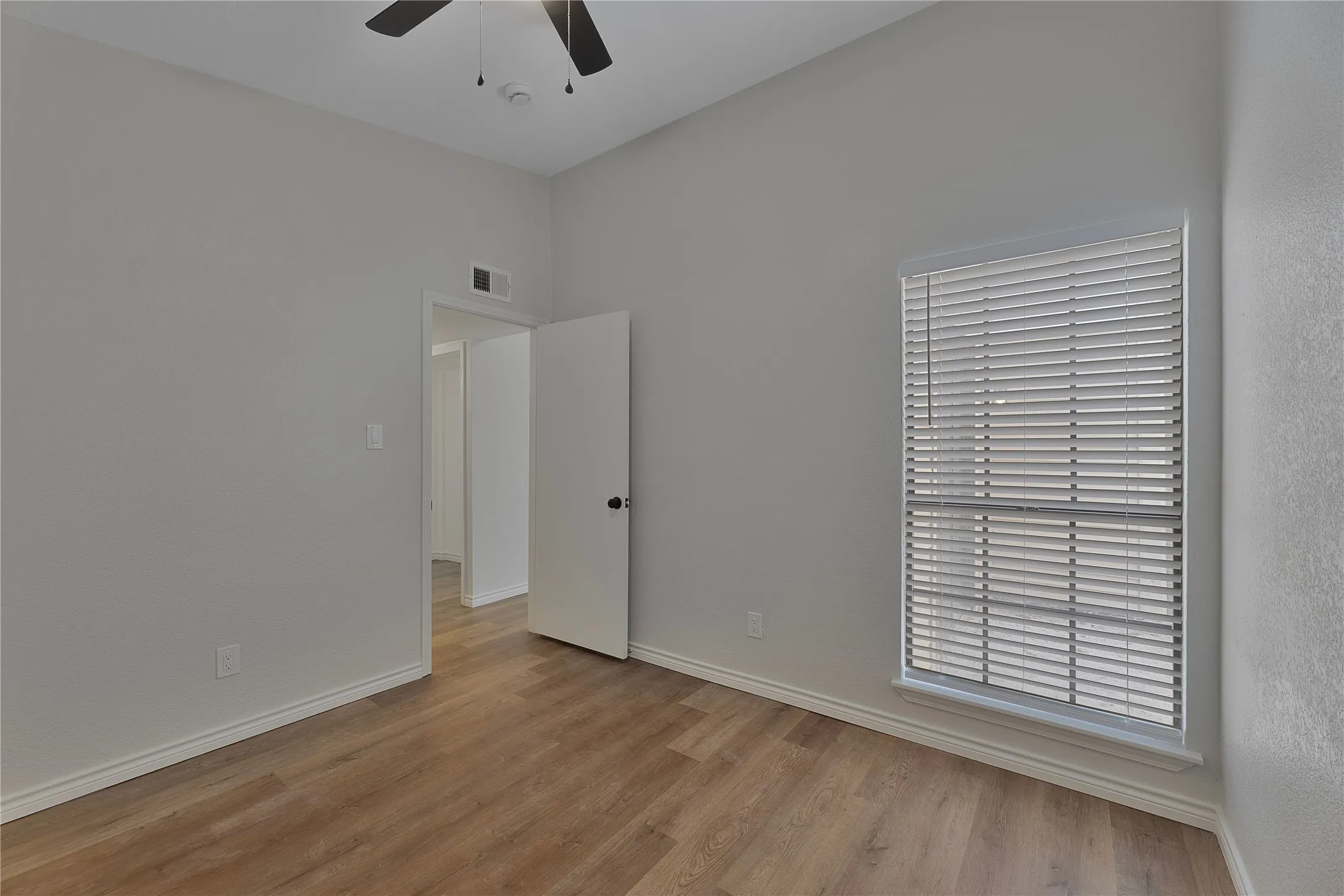 Room featuring wood-finish flooring, light gray walls, white trim, and a ceiling fan