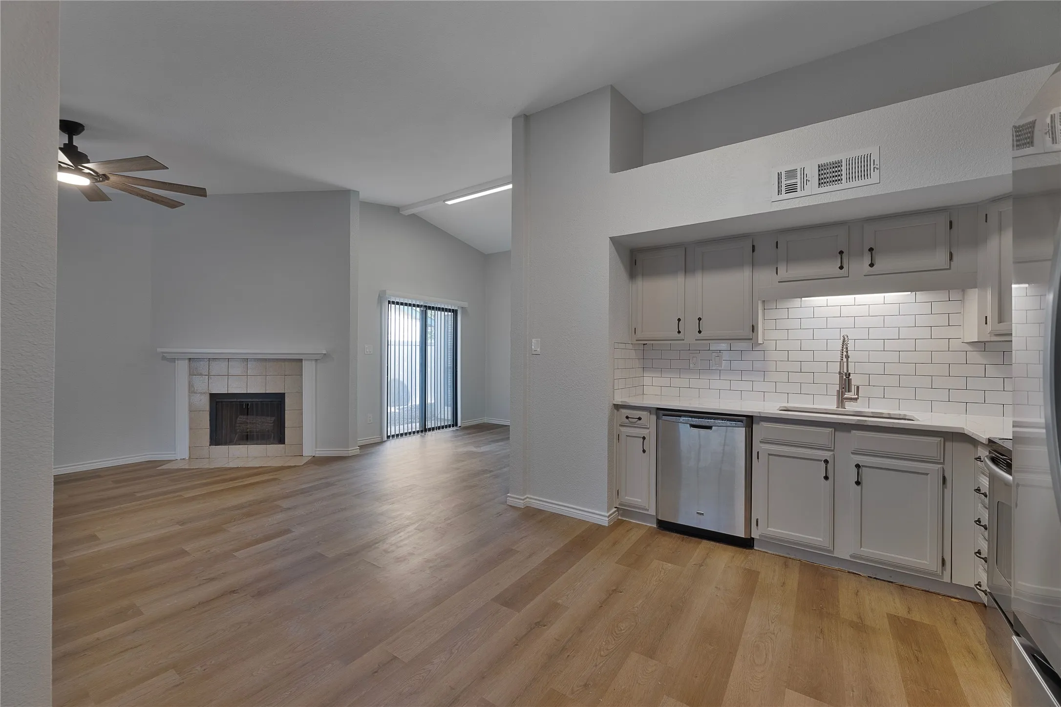 Open-concept living space featuring wood-finish flooring, a tiled fireplace, and a vaulted ceiling