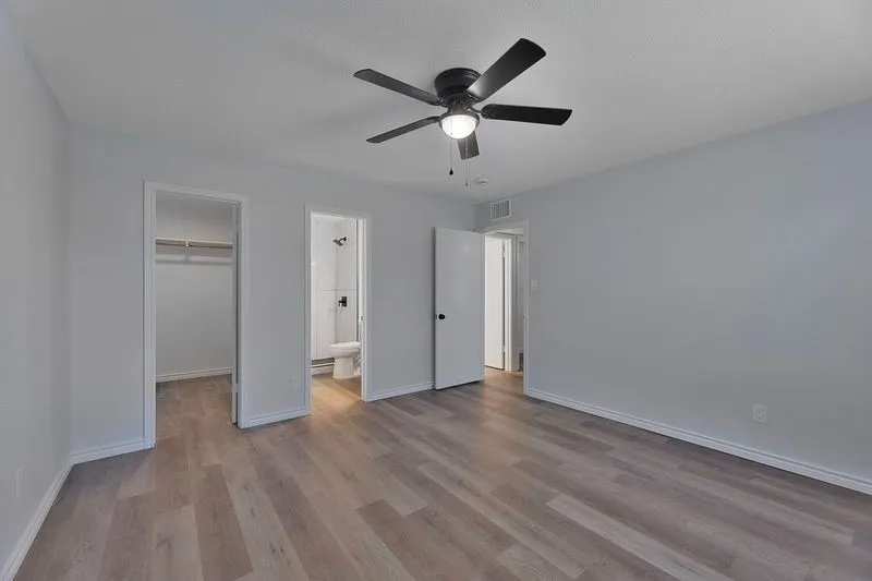 Spacious room featuring wood-finish flooring, a contemporary ceiling fan with integrated lighting, and light gray painted walls