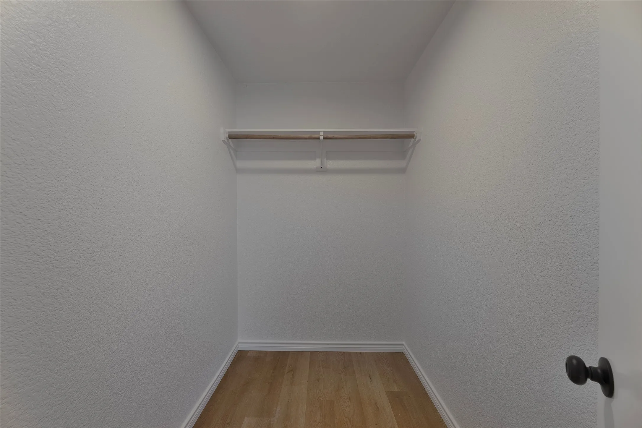Walk-in closet with wood-finish flooring, white baseboards, and a single-rod hanging system