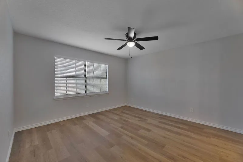 Spacious room featuring wood-finish flooring, a contemporary ceiling fan with integrated lighting, and a window with blinds