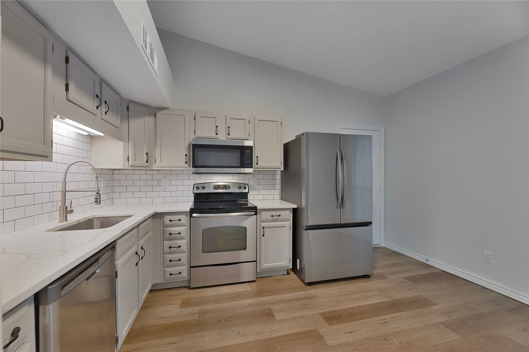 Contemporary kitchen featuring wood-finish flooring, white subway tile backsplash, and light gray cabinetry