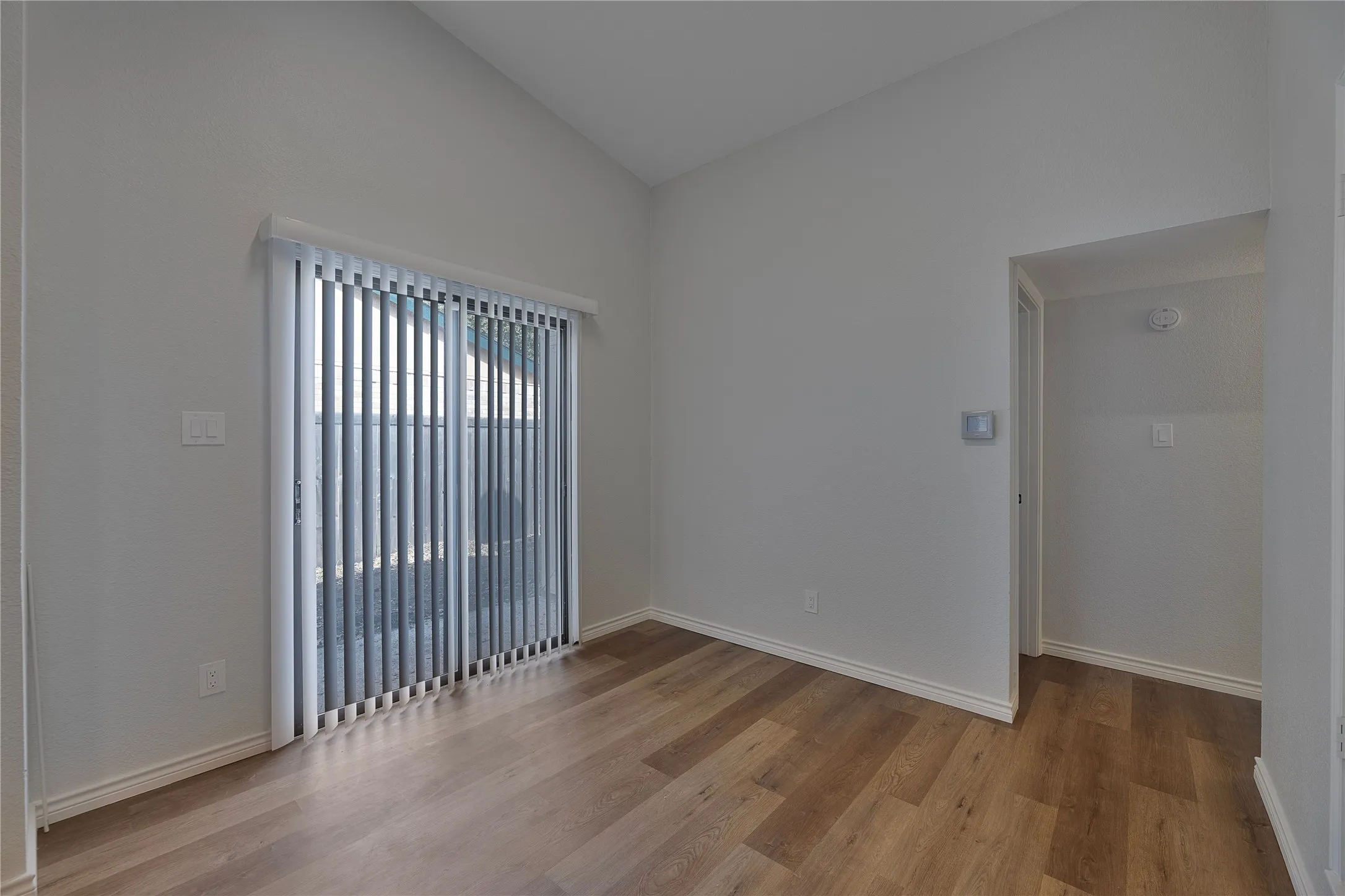 Vaulted ceiling room with wood-finish flooring, light gray walls, and white baseboards