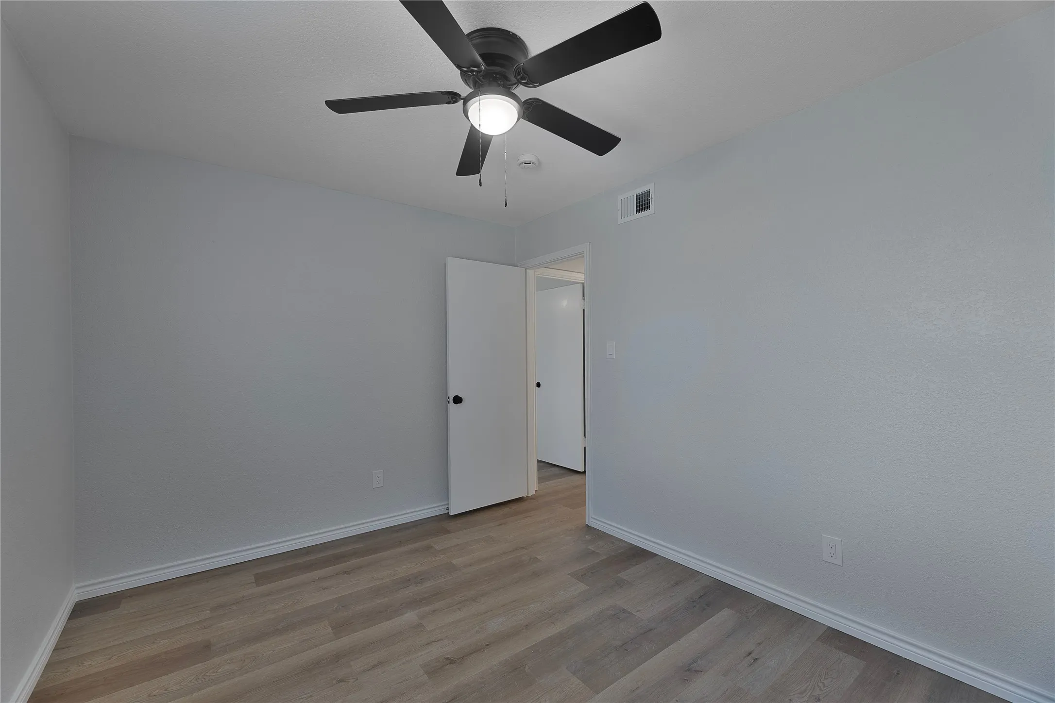 Spacious room with light gray walls, wood-finish flooring, and crisp white baseboards