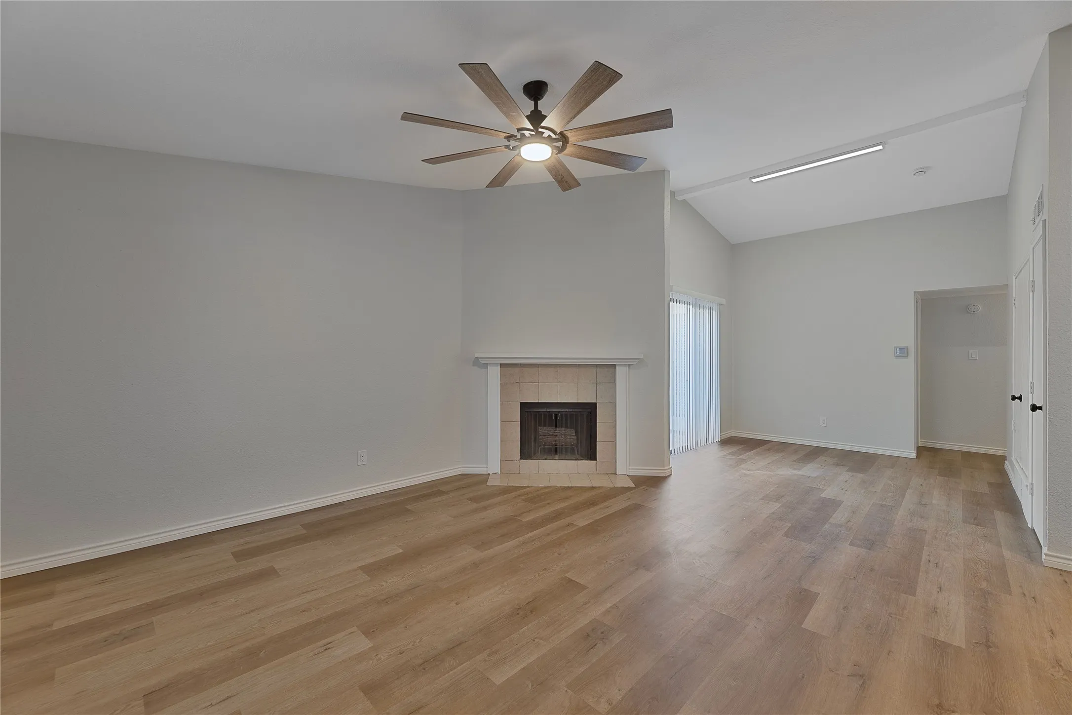 Spacious room featuring wood-finish flooring, a tile-surround fireplace with a mantel, and a vaulted ceiling with a ceiling fan