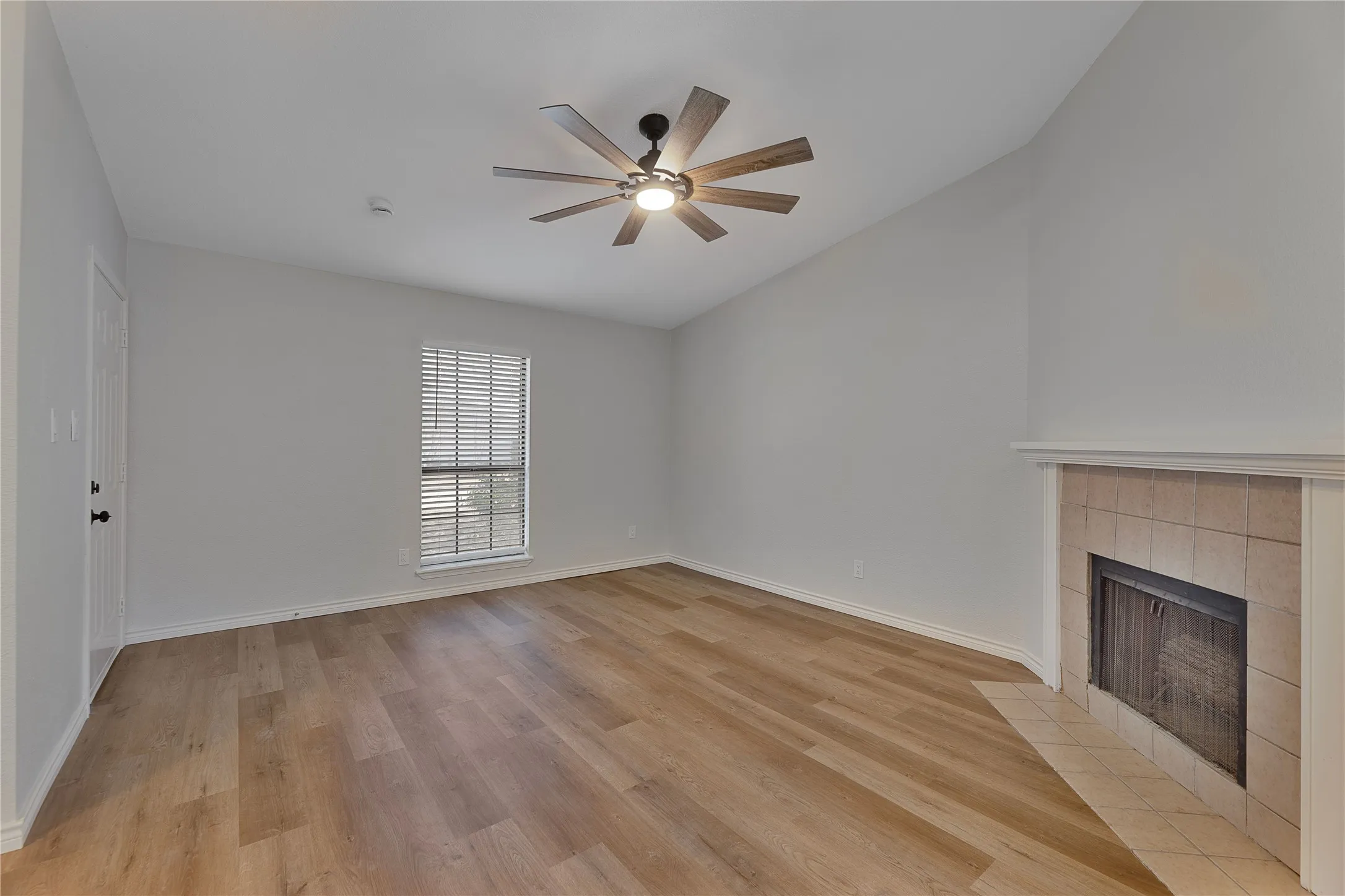 Spacious room featuring wood-finish flooring, an angled ceiling, and a fireplace with a tiled hearth and surround