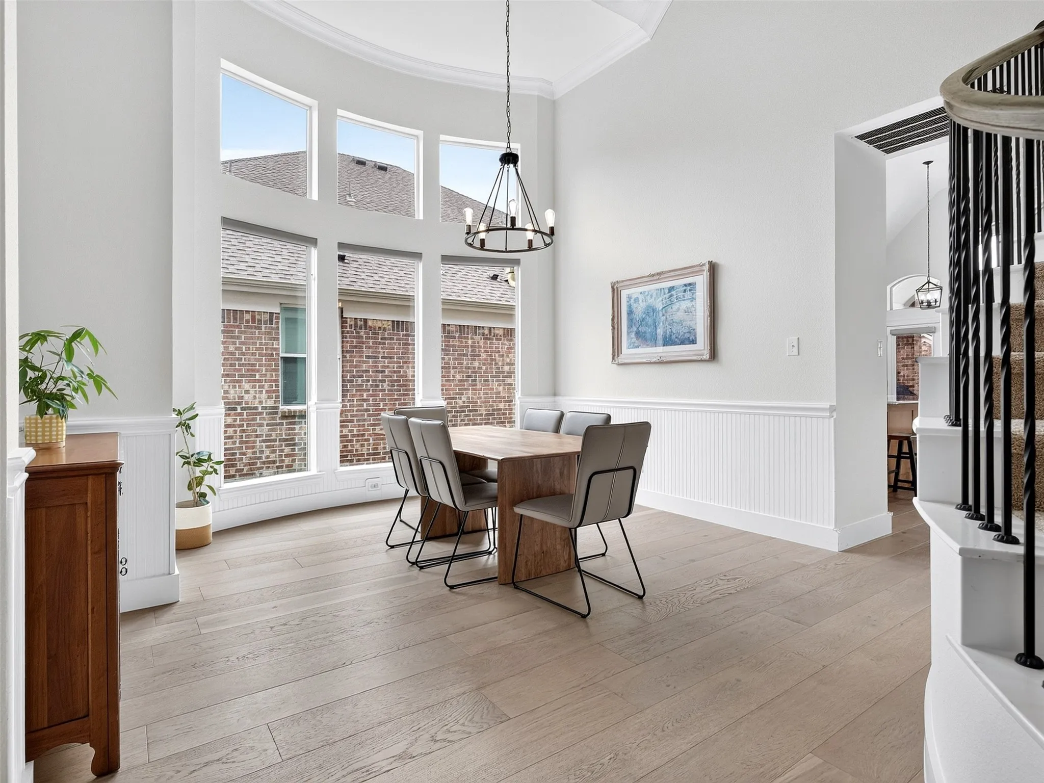 Two-story dining space featuring an arched window wall, wood-finish flooring, wainscoting, and a candelabra chandelier