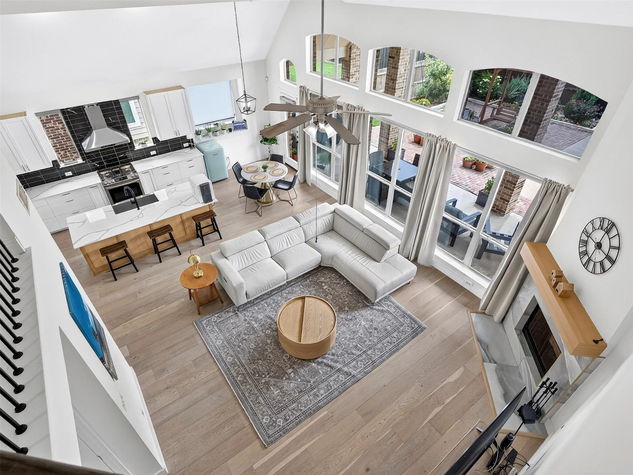 High-ceiling living space featuring extensive windows, wood-finish flooring, and an integrated kitchen