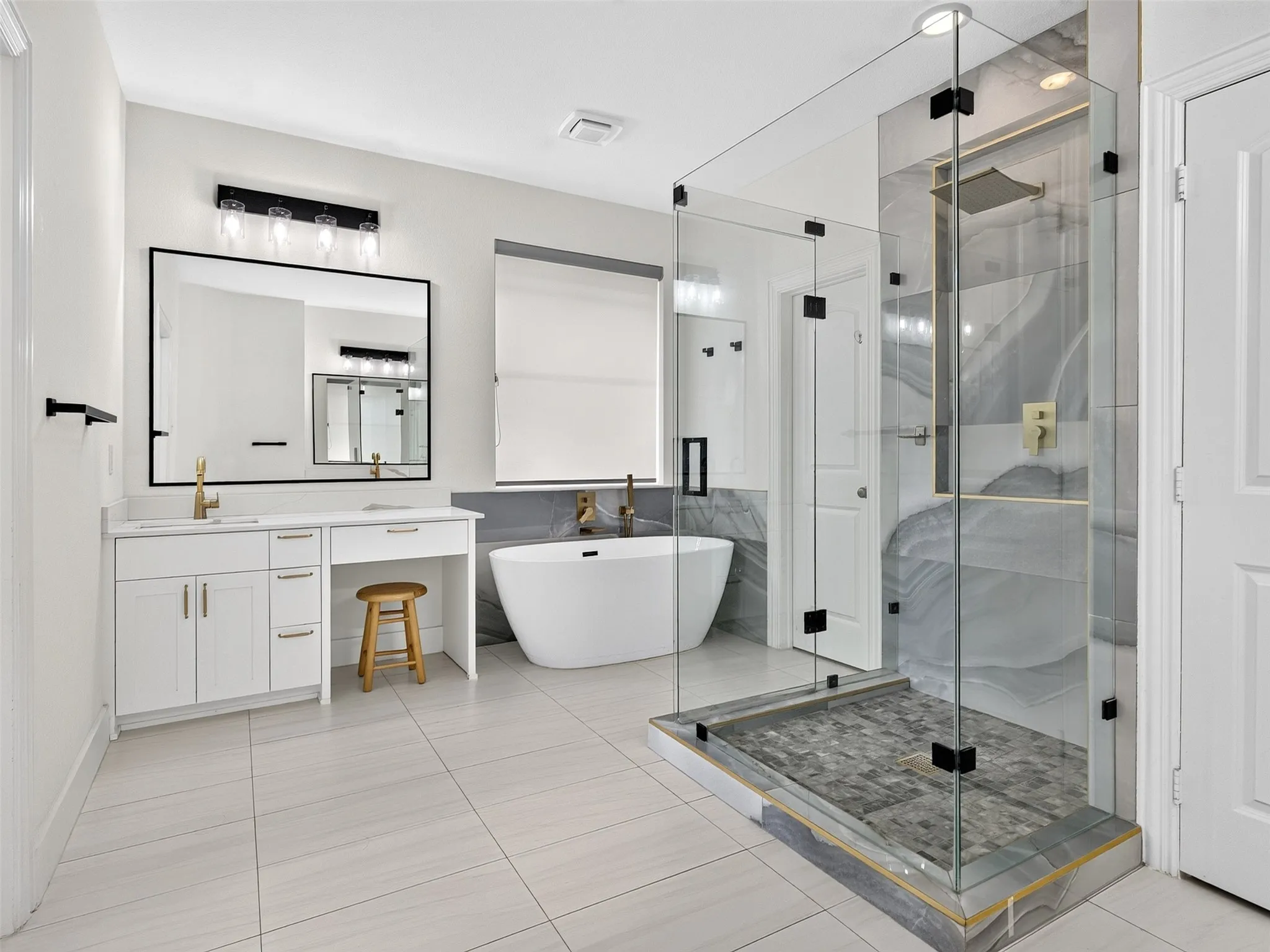 Glass-enclosed shower with contrasting large-format tile, freestanding soaking tub, and a double vanity with stone countertops