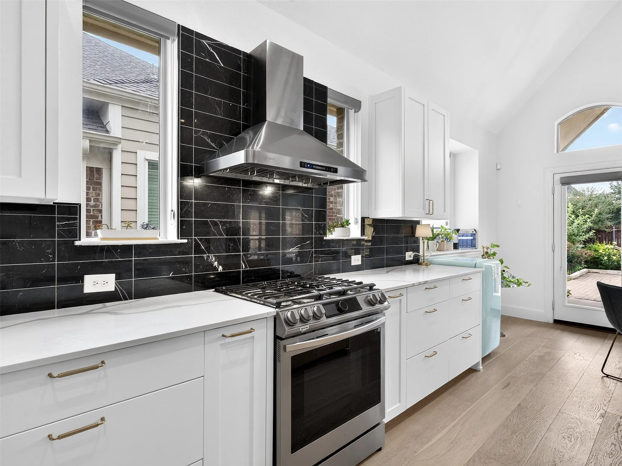 Modern kitchen featuring a stainless steel gas range, coordinating range hood, and white shaker-style cabinetry