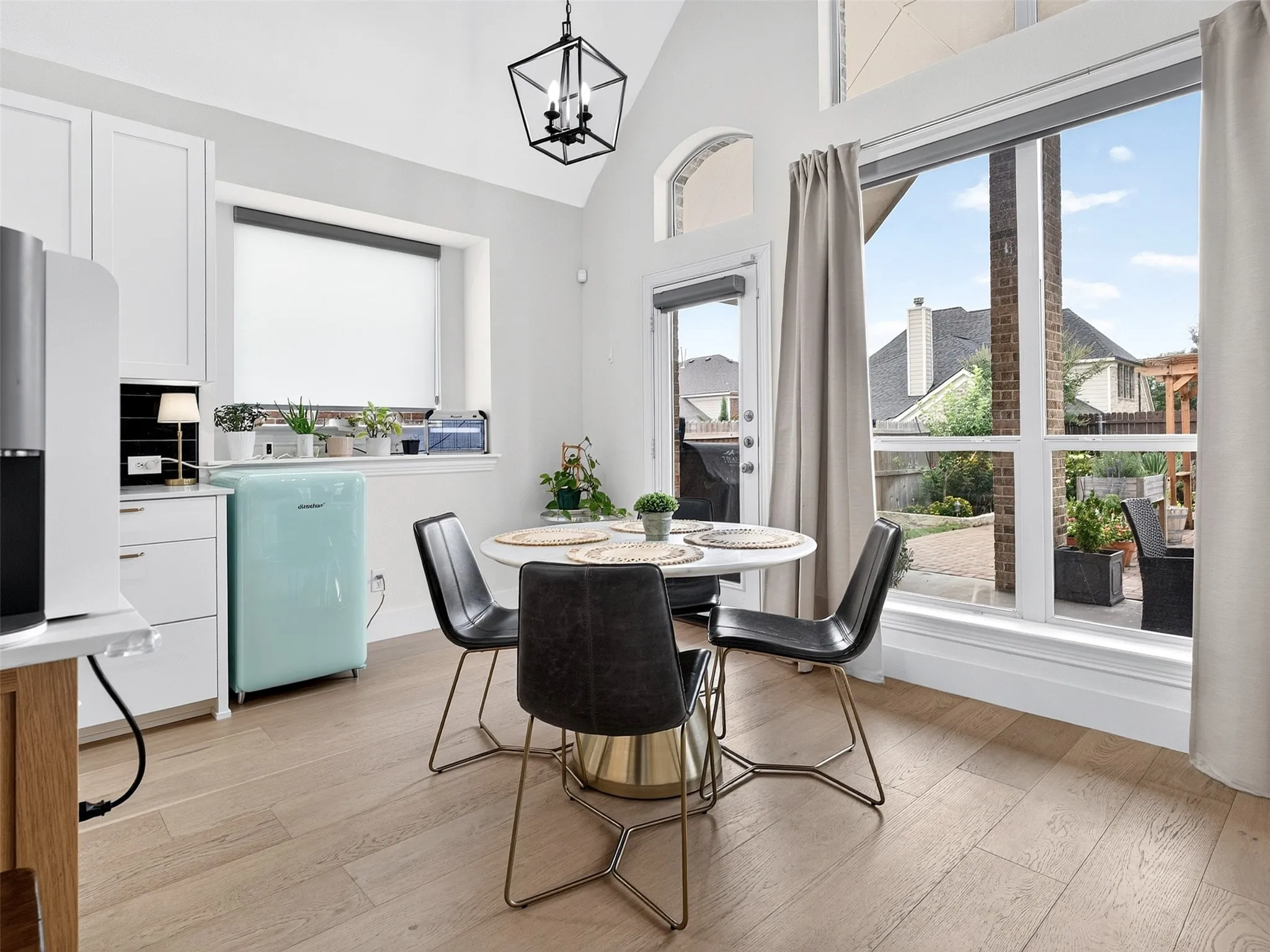 Bright dining area featuring wood-finish flooring, white cabinetry, and a black geometric light fixture