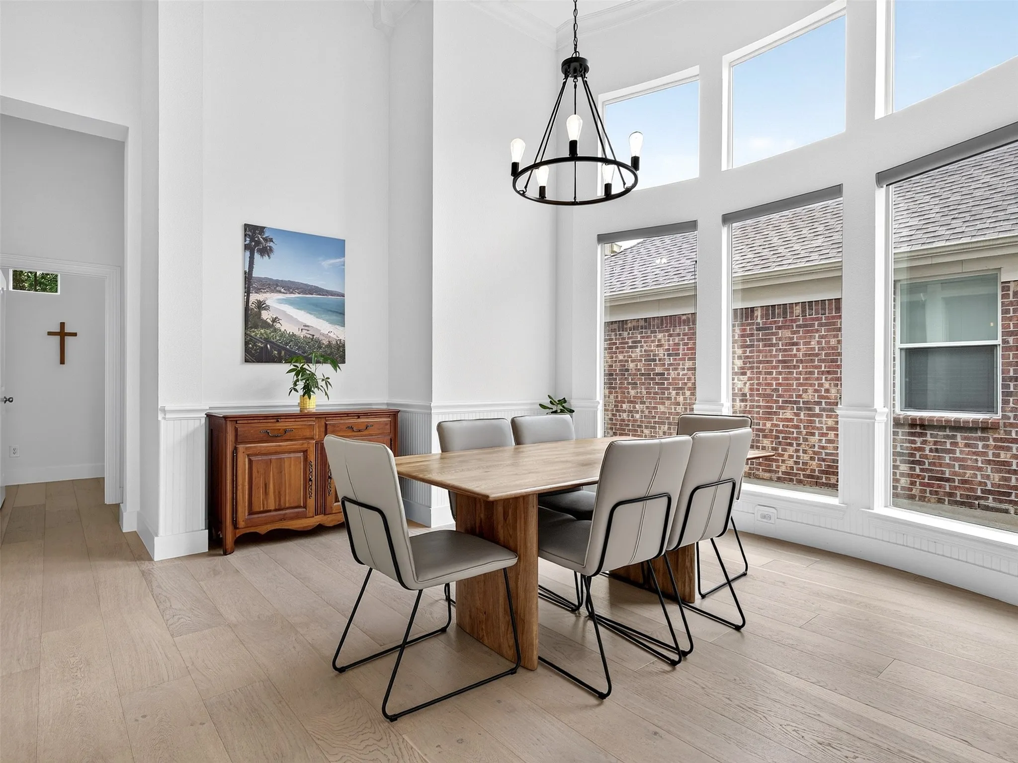 Two-story dining space featuring expansive windows, wood-finish flooring, a contemporary chandelier, white wainscoting, and crisp white walls