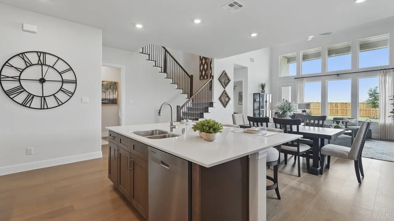 Open-concept living area featuring wood-finish flooring, a kitchen island with a stainless steel sink and integrated dishwasher, a formal dining space, and a two-story wall of windows