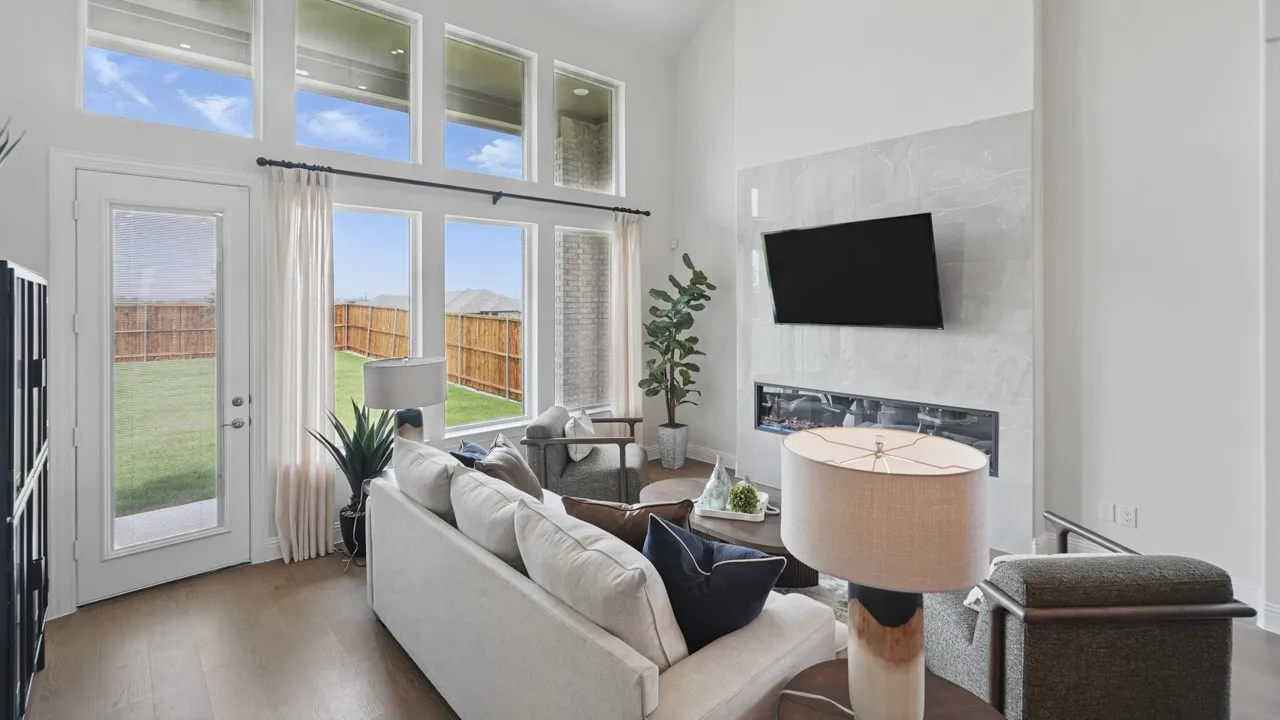 Two-story living area with wood-finish flooring, a contemporary fireplace featuring a stone-look surround, and a wall of windows including transom windows
