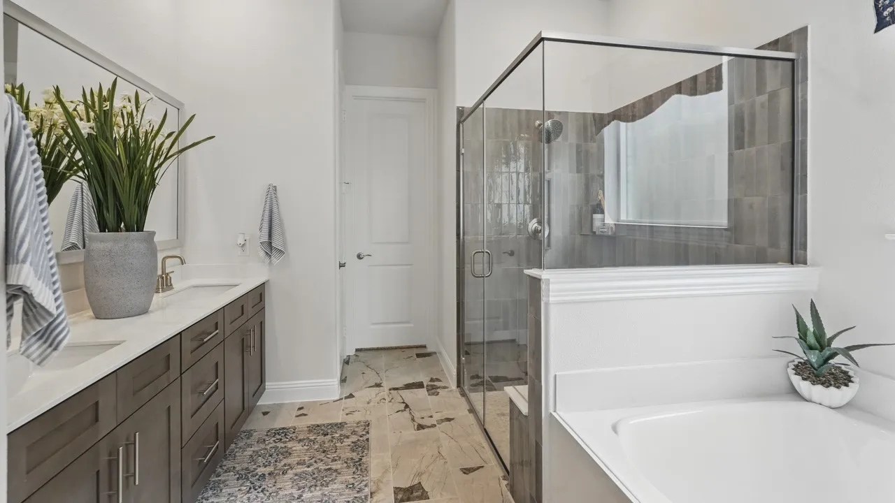 Bathroom featuring a double vanity with stone countertops, a frameless glass shower enclosure with tile surround, a built-in bathtub, and mosaic tile flooring