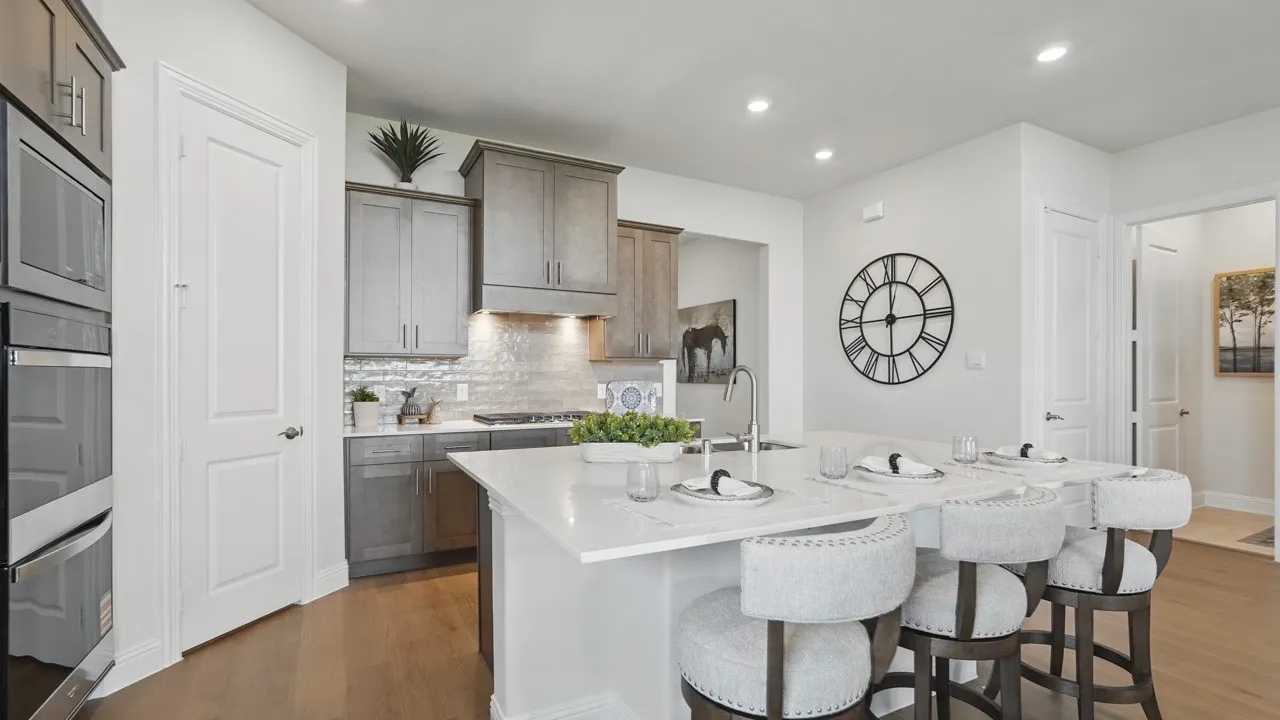Modern kitchen featuring an expansive island with a white countertop and seating, stainless steel double ovens, gray wood-finish cabinetry, a subway tile backsplash, and recessed lighting