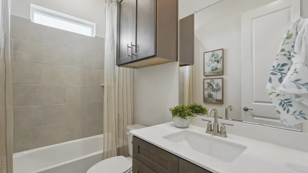 Bathroom featuring a built-in tub with large format tile surround, transom window, wood-finish vanity with an integrated sink, polished chrome faucet, and a large wall mirror