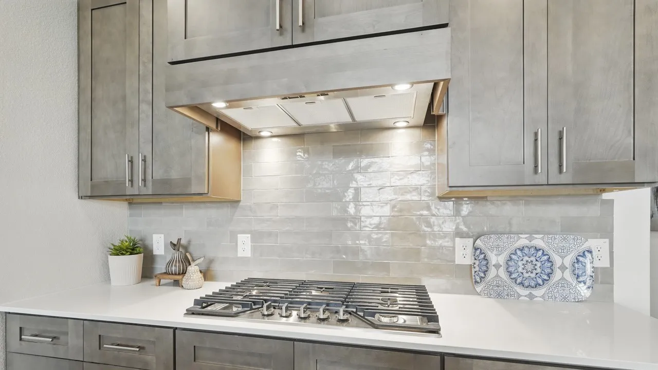 Integrated gas cooktop with a range hood featuring recessed lighting, set against a subway tile backsplash