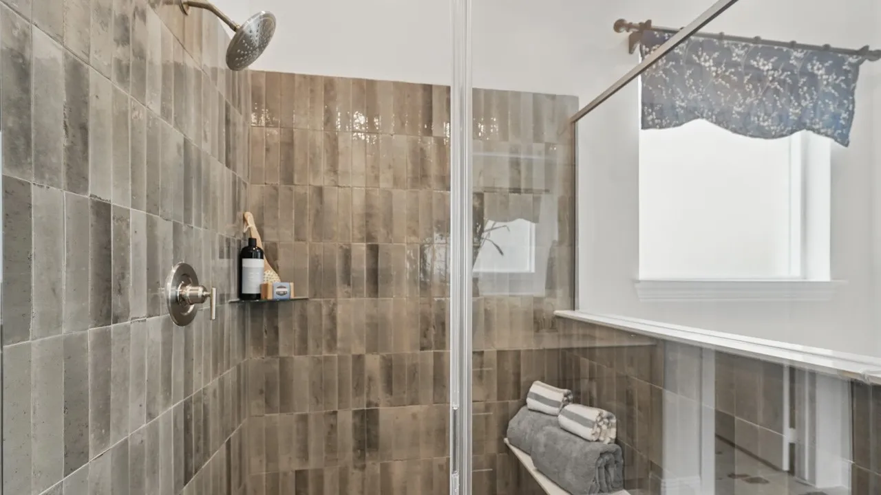 Shower enclosure featuring full-height tiled walls, a rain shower head, and a built-in shower bench