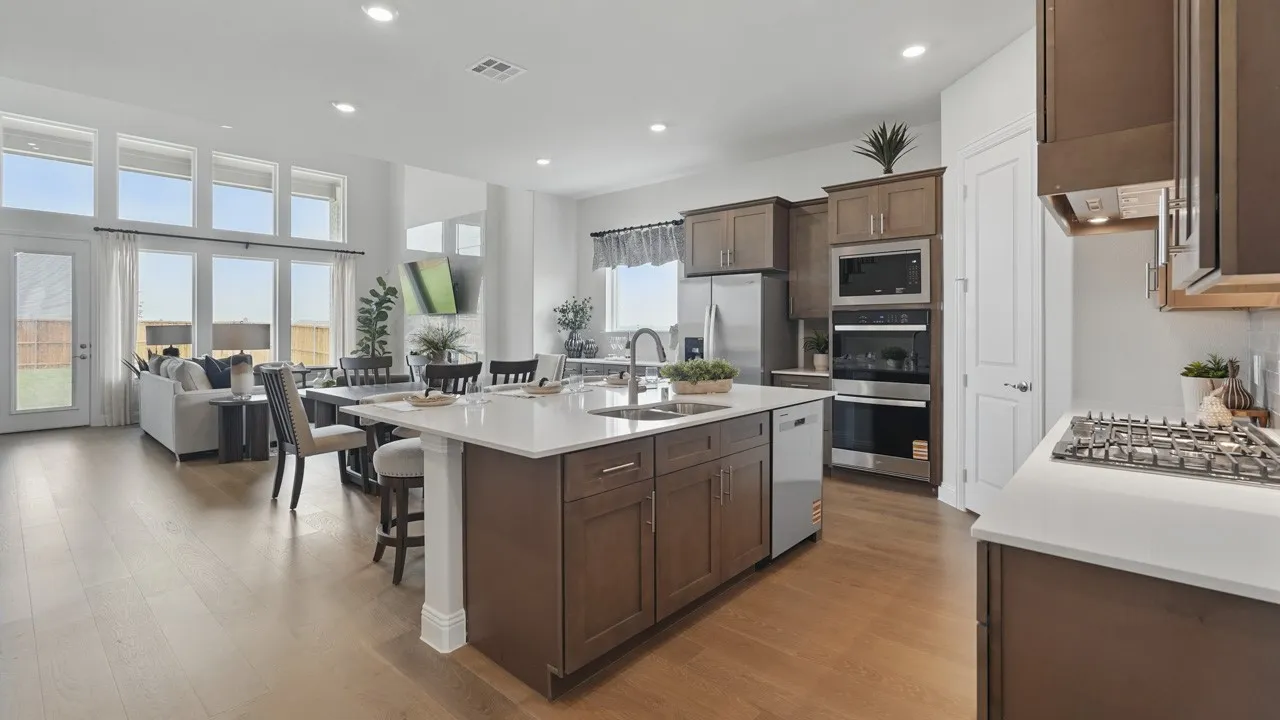 Open-concept living space featuring wood-finish flooring, a large kitchen island with integrated sink and dishwasher, stainless steel appliances, and a wall of windows offering exterior access