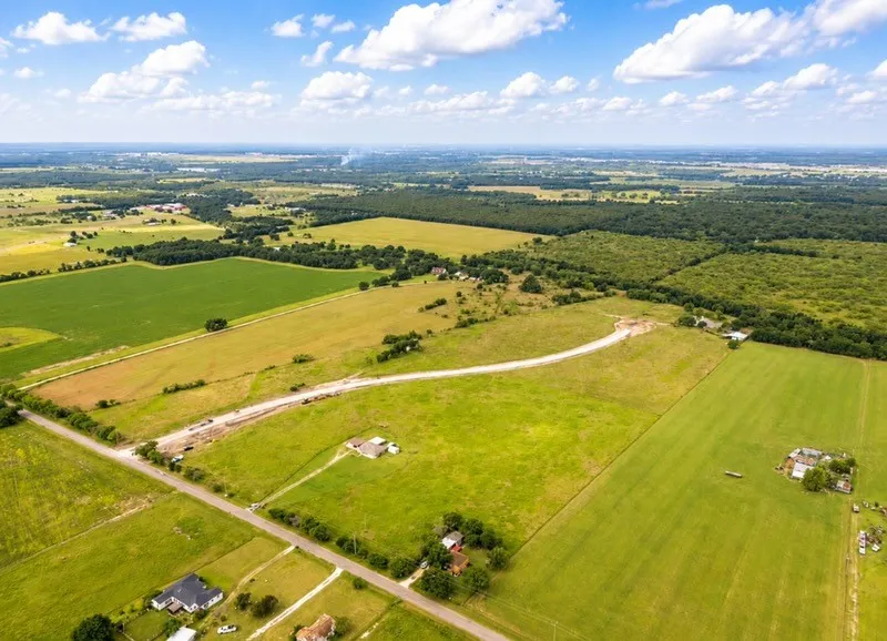 Expansive aerial landscape featuring multiple green fields, a paved road, and sections of mature treelines