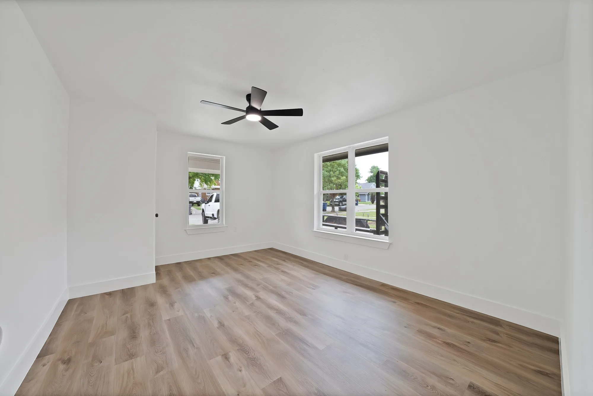 Spacious room featuring wood-finish flooring, white walls, and a contemporary ceiling fan with integrated lighting