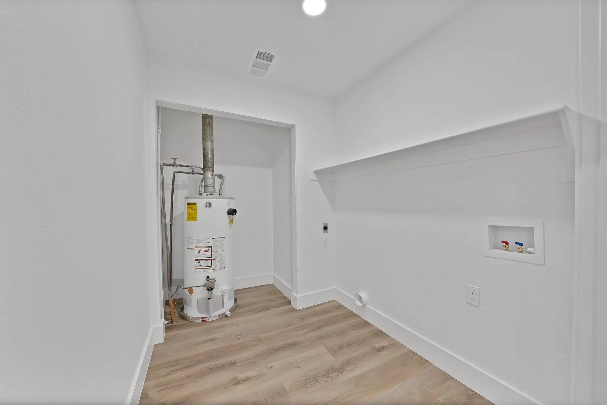 Utility area with a water heater, wood-finish flooring, a wall shelf, and appliance hookups