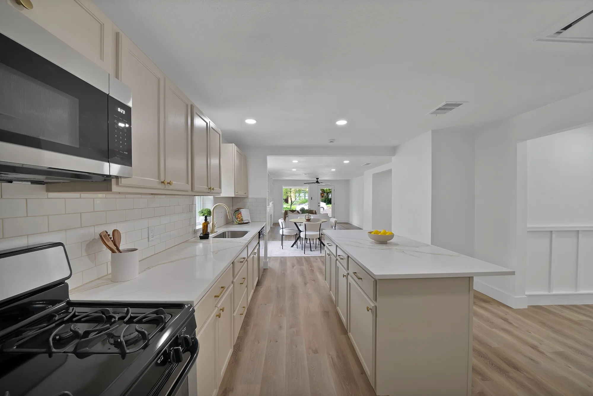 Galley kitchen featuring light-toned cabinetry, stainless steel appliances, a subway tile backsplash, and light wood-finish flooring