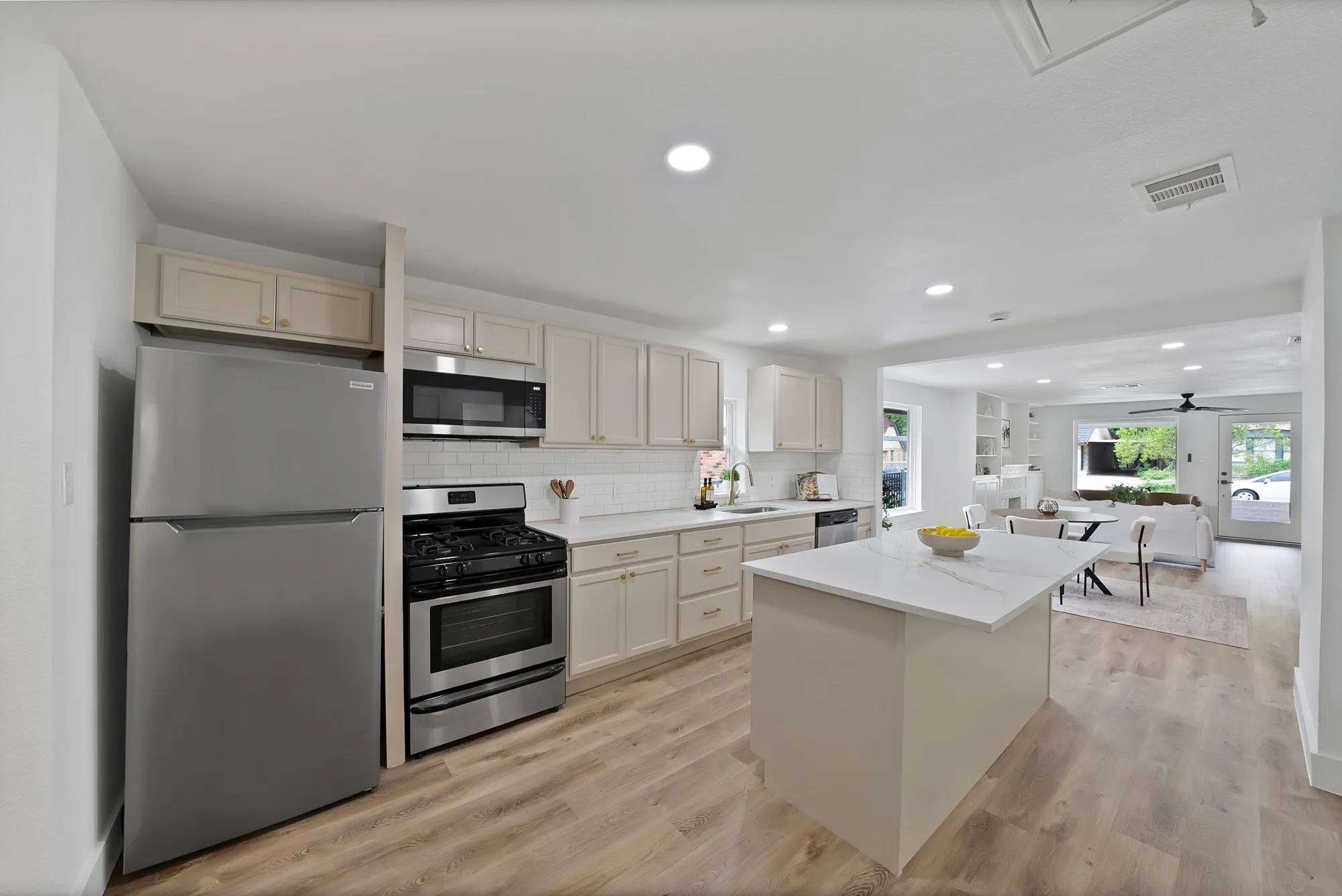 Contemporary kitchen featuring a central island with a light-toned countertop, stainless steel appliances, light-toned cabinetry, and wood-finish flooring