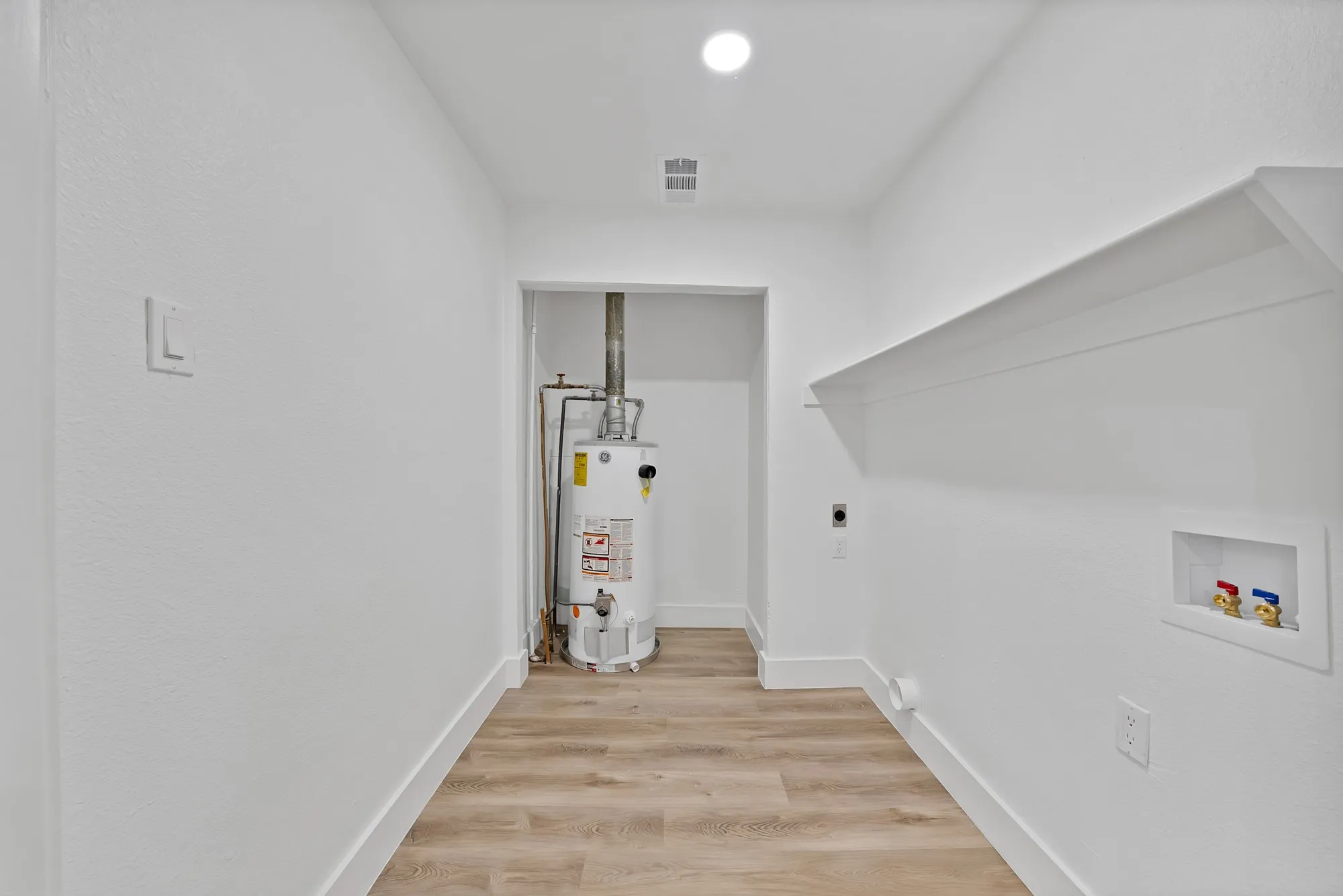 Dedicated utility space featuring wood-finish flooring, a built-in shelf, and crisp white walls
